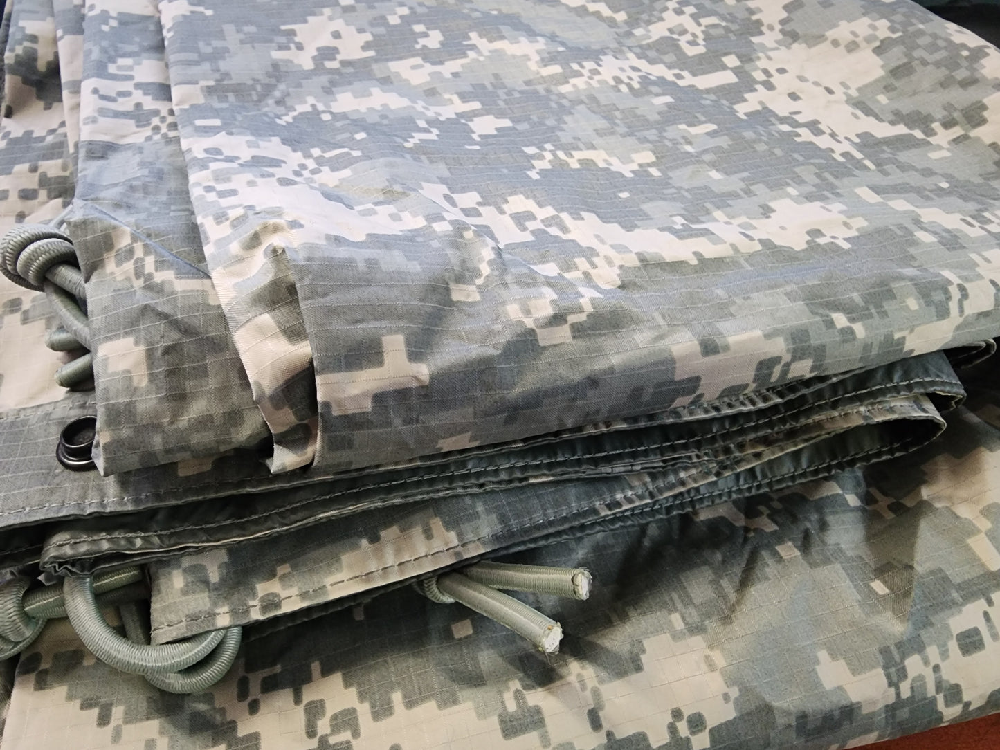 A green camouflage tarp with reinforced edges and multiple tie-down points.