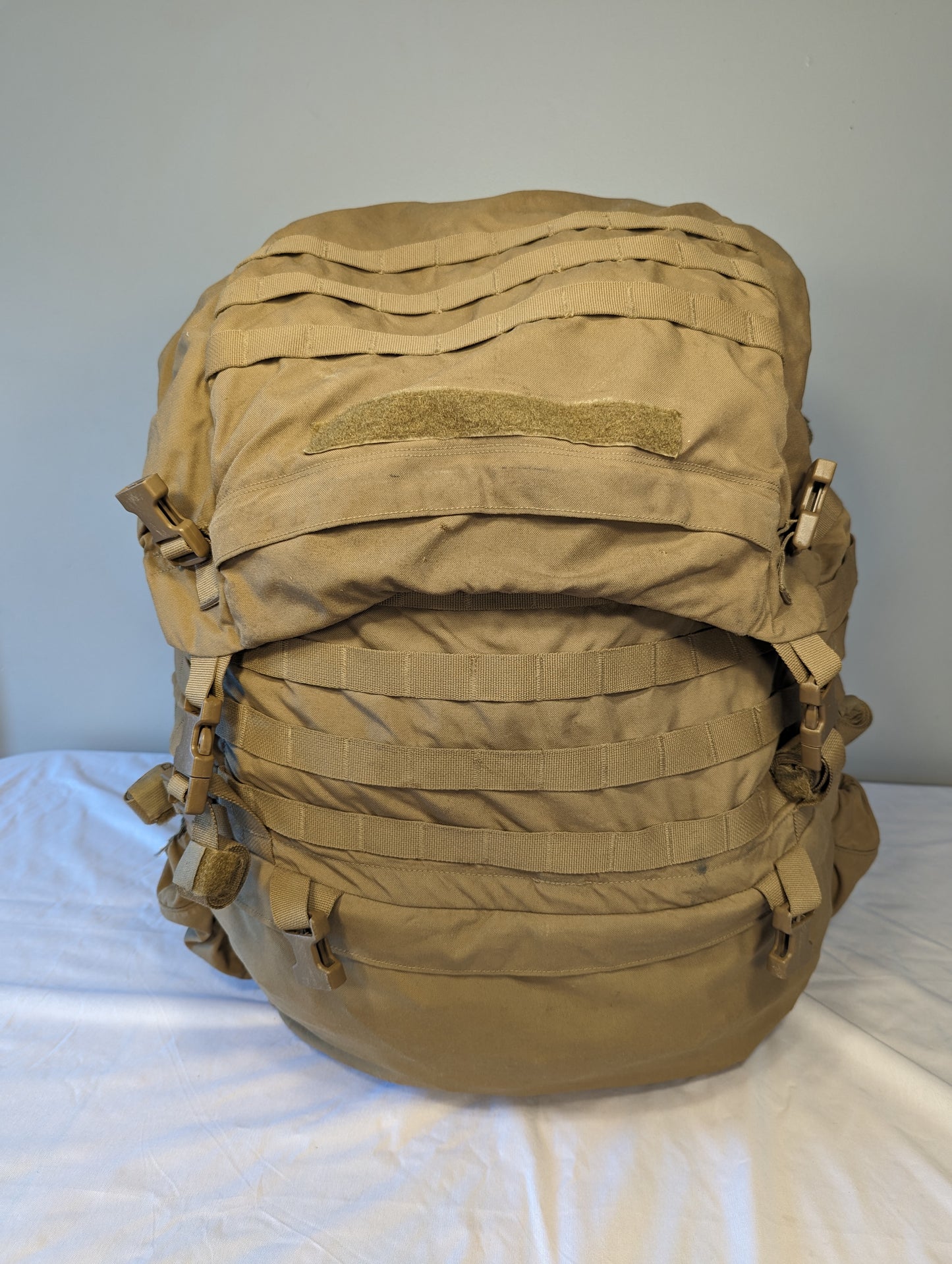 Tan military-style backpack on a white surface with a gray background