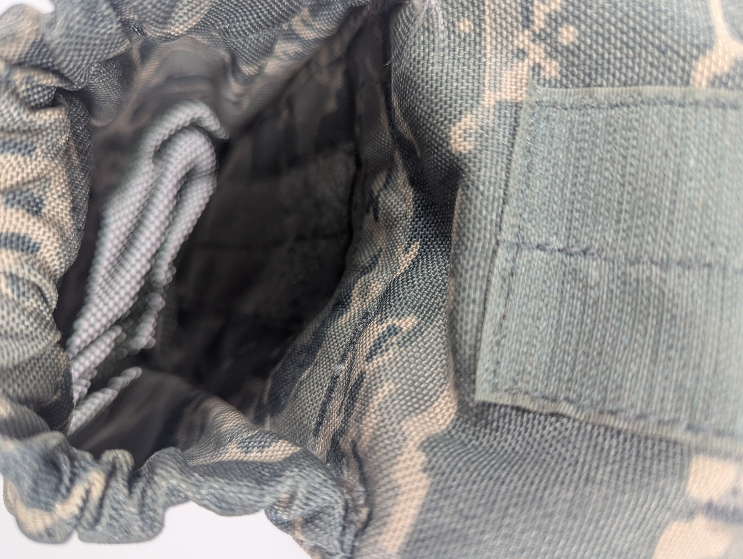 Close-up of a camouflage fabric pouch or pocket showing the interior lining and exterior texture in a gray, green, and tan pattern.