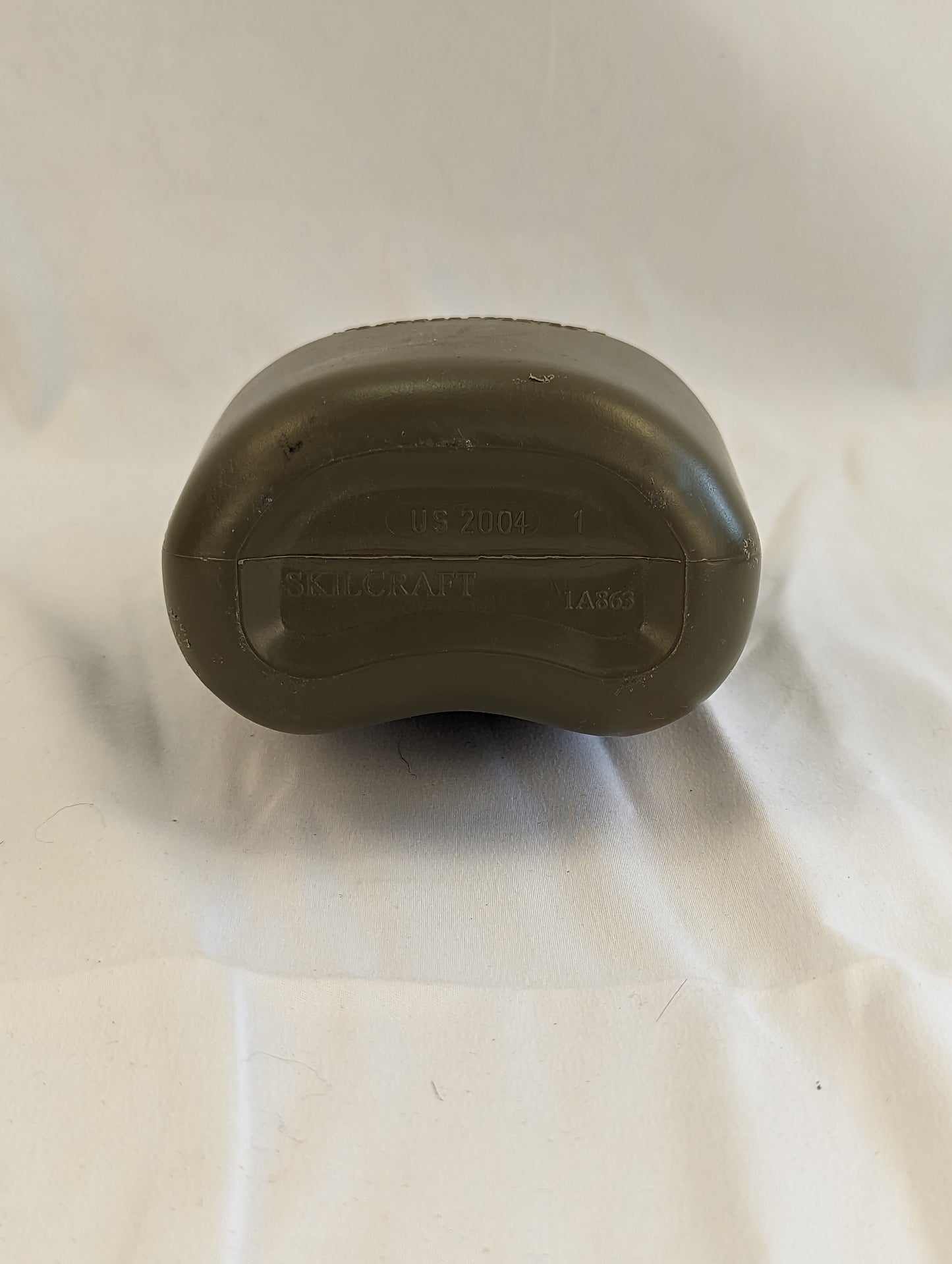 A close-up studio shot of the bottom of a used U.S. Military Surplus 1-quart plastic canteen in olive green, showing its molded plastic base and capacity markings against a wrinkled white background.