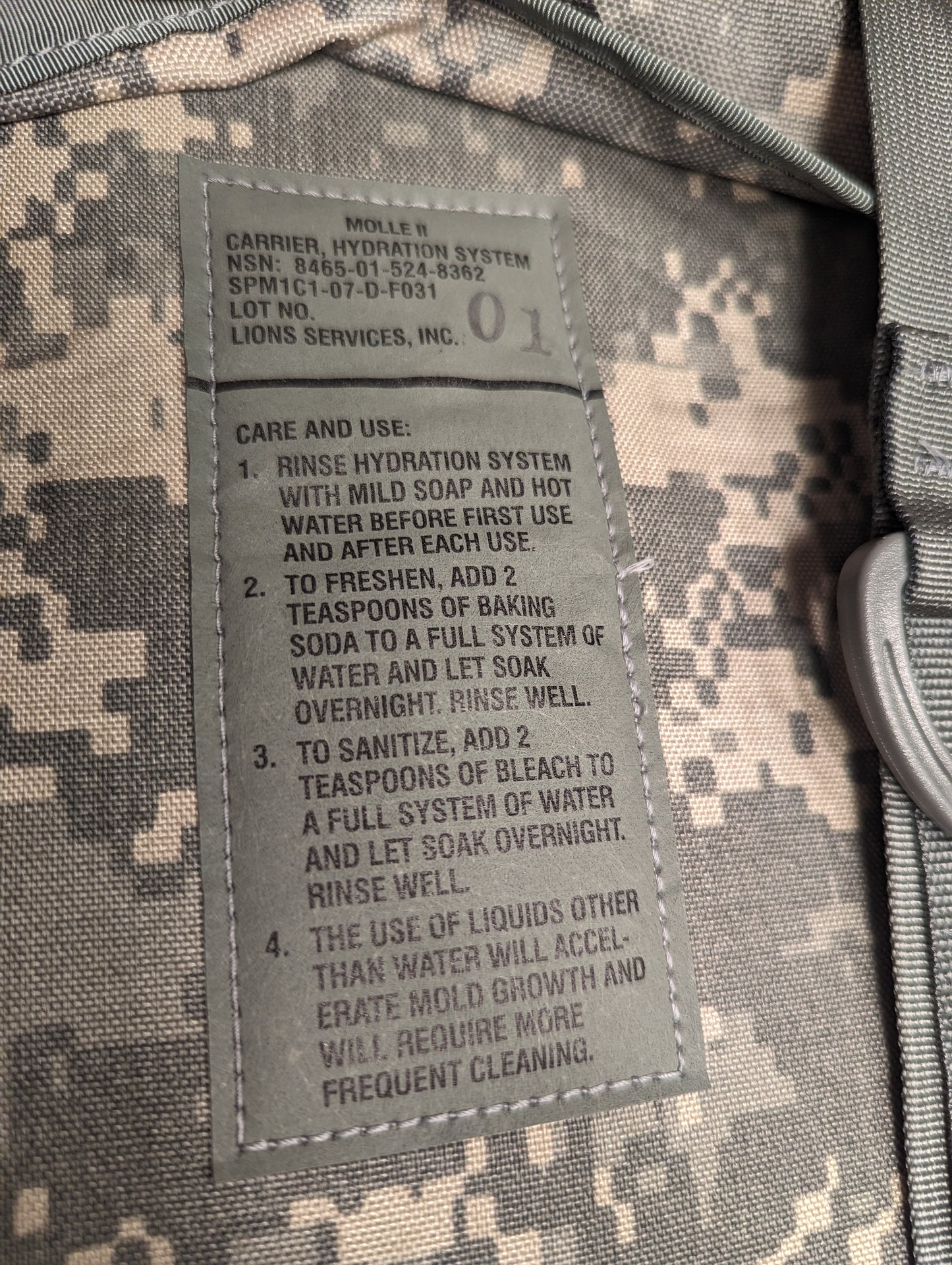 A close-up photograph of the U.S. Military Hydration Carrier care tag, displaying detailed cleaning and sanitizing instructions using mild soap, baking soda, and bleach, with a mold warning.