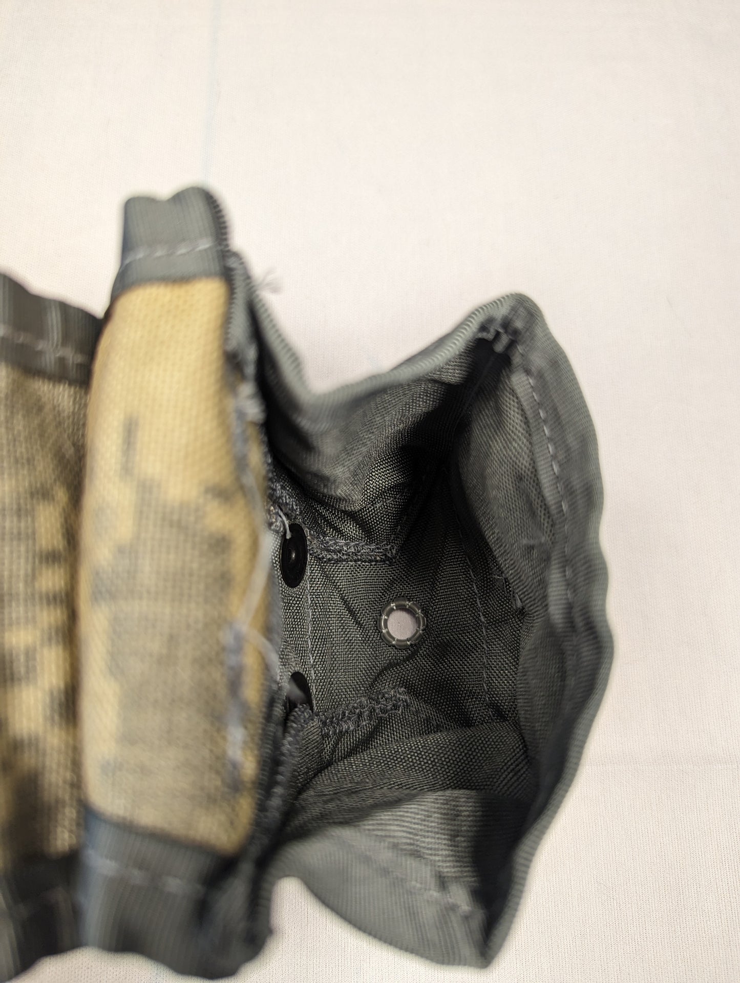 A close-up overhead view looking inside an open U.S. Military Surplus Hand Grenade Pouch in ACU digital camouflage, revealing the empty interior compartment, snap buttons, and a metal drainage grommet at the bottom.