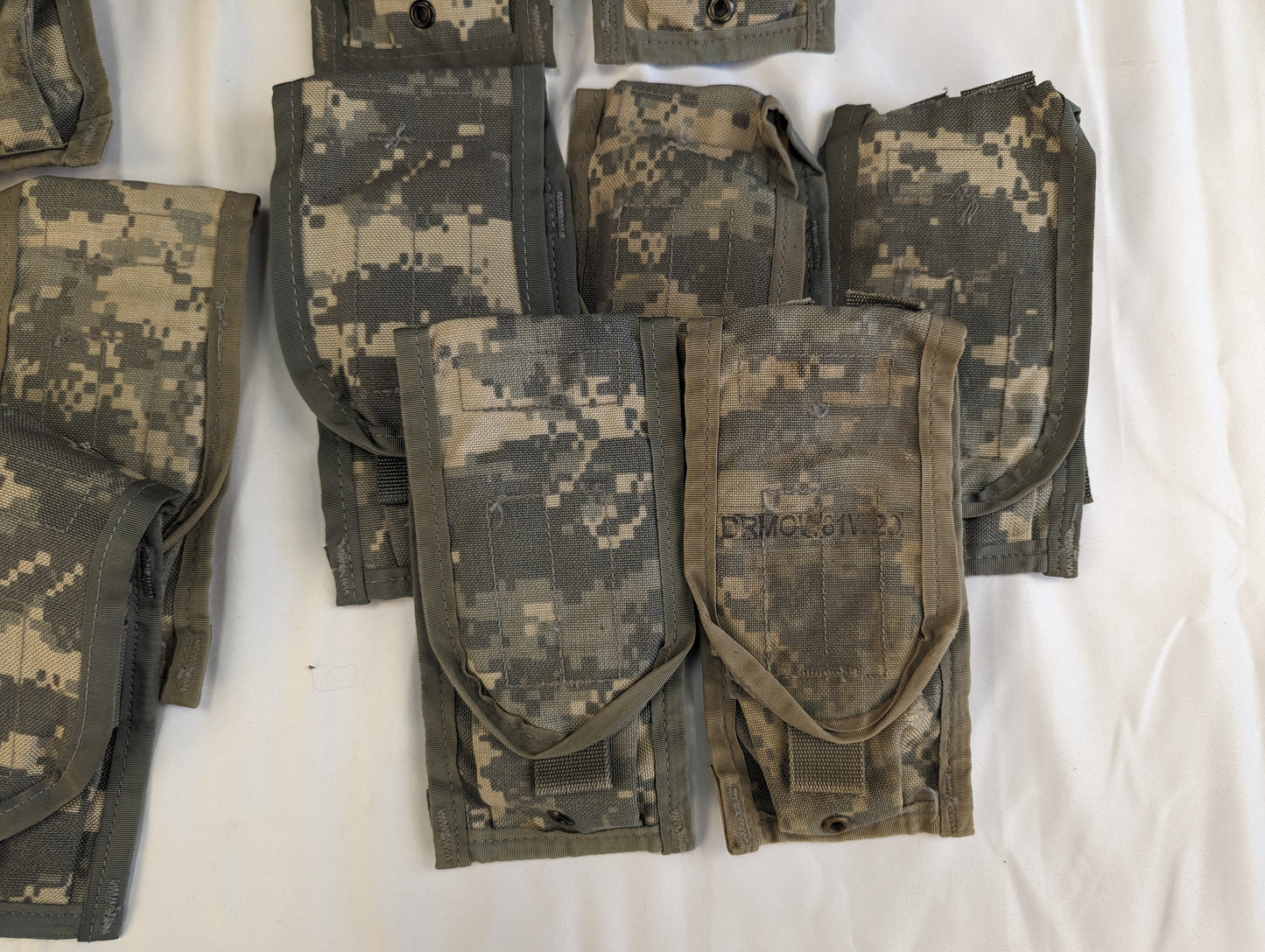 A close-up studio shot of a cluster of overlapping U.S. Military Surplus 2-Mag Pouches in ACU digital camouflage, highlighting the worn flaps, snap closures, and used fabric texture.