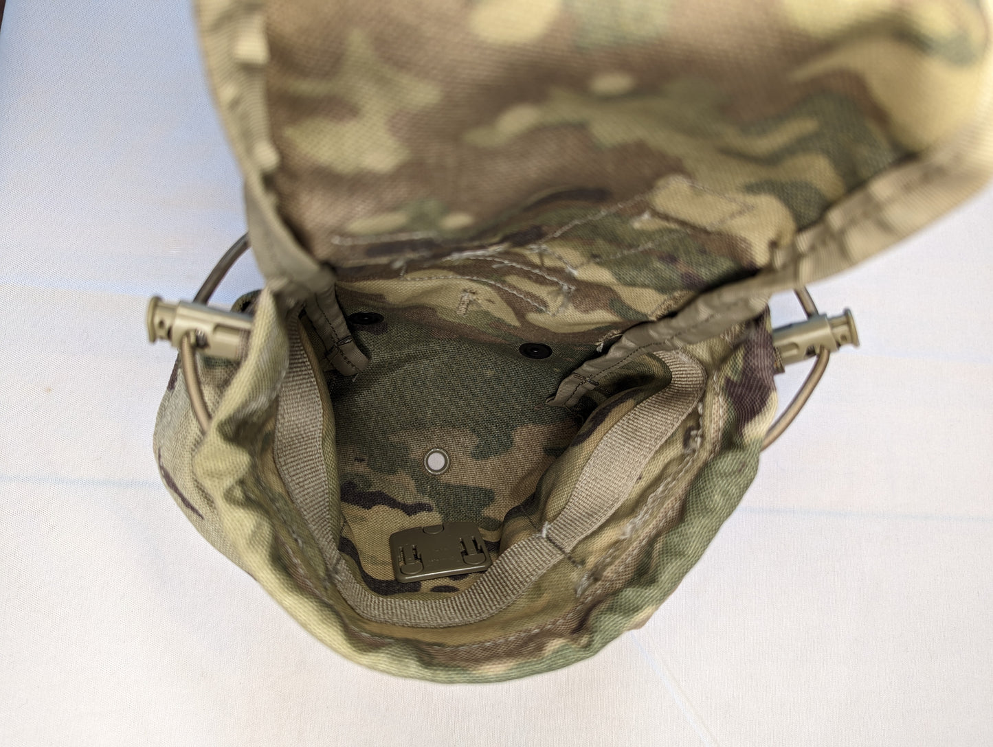 A close-up, high-angle view looking into the open interior of a U.S. Military Surplus Canteen/General Purpose Pouch in OCP/Multicam camouflage, revealing the empty internal space, side attachment loops, and a drainage grommet.