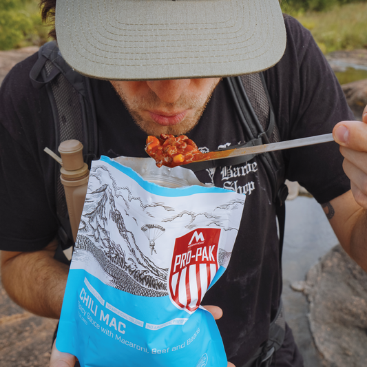 Person eating from a Pro-Pak Chili Mac package outdoors