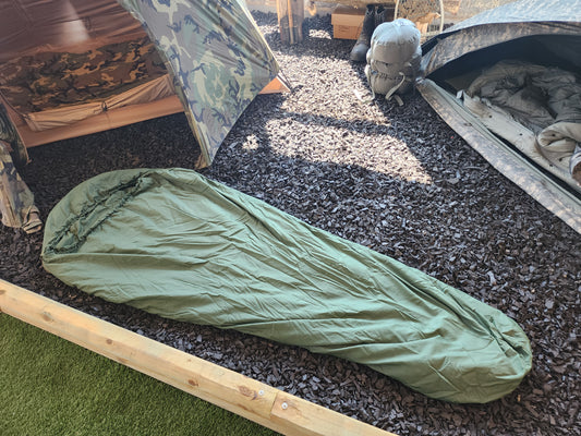 Green sleeping bag on the ground next to a tent in an outdoor setting
