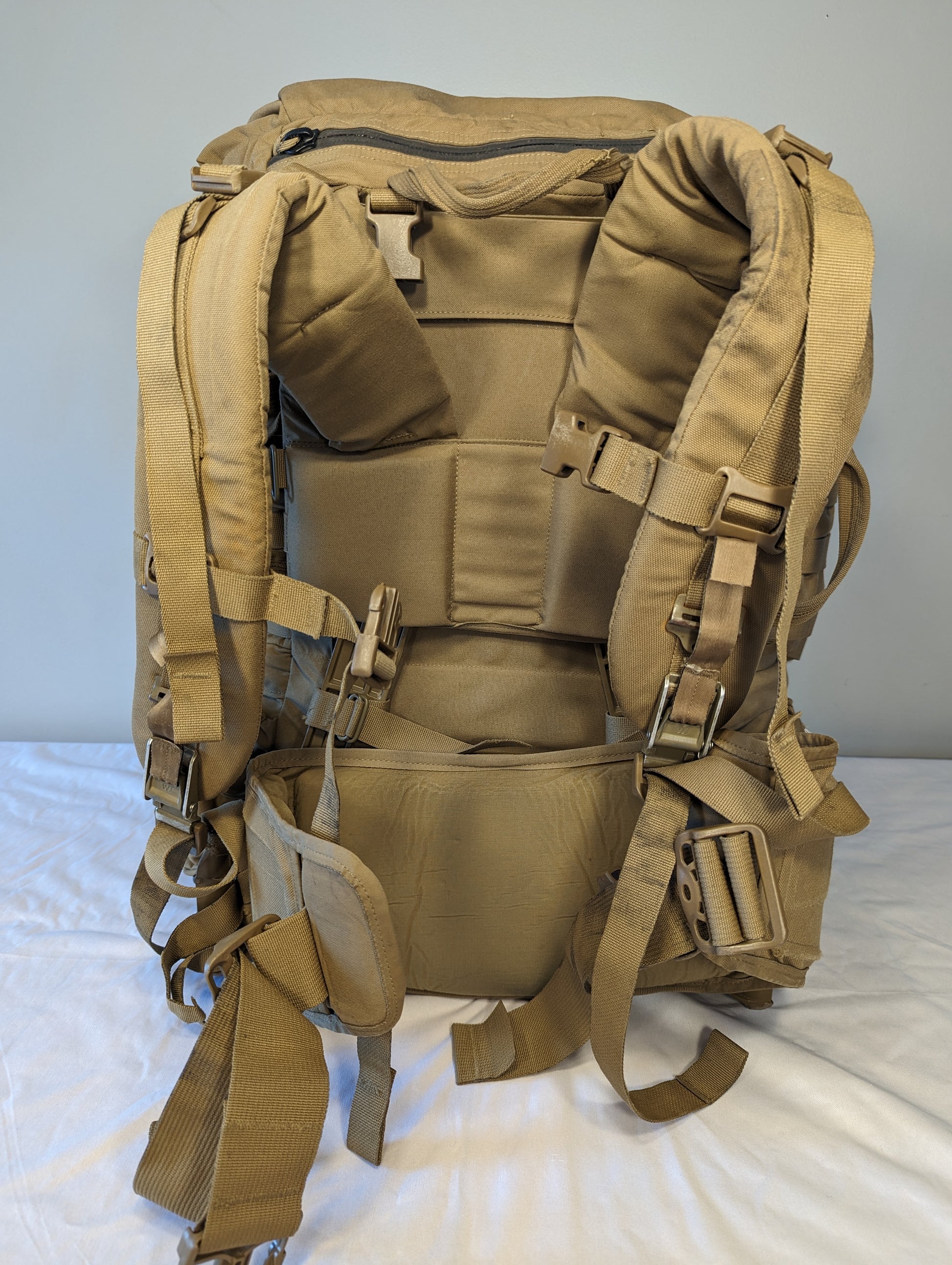 Tan military-style backpack on a white surface with a gray background