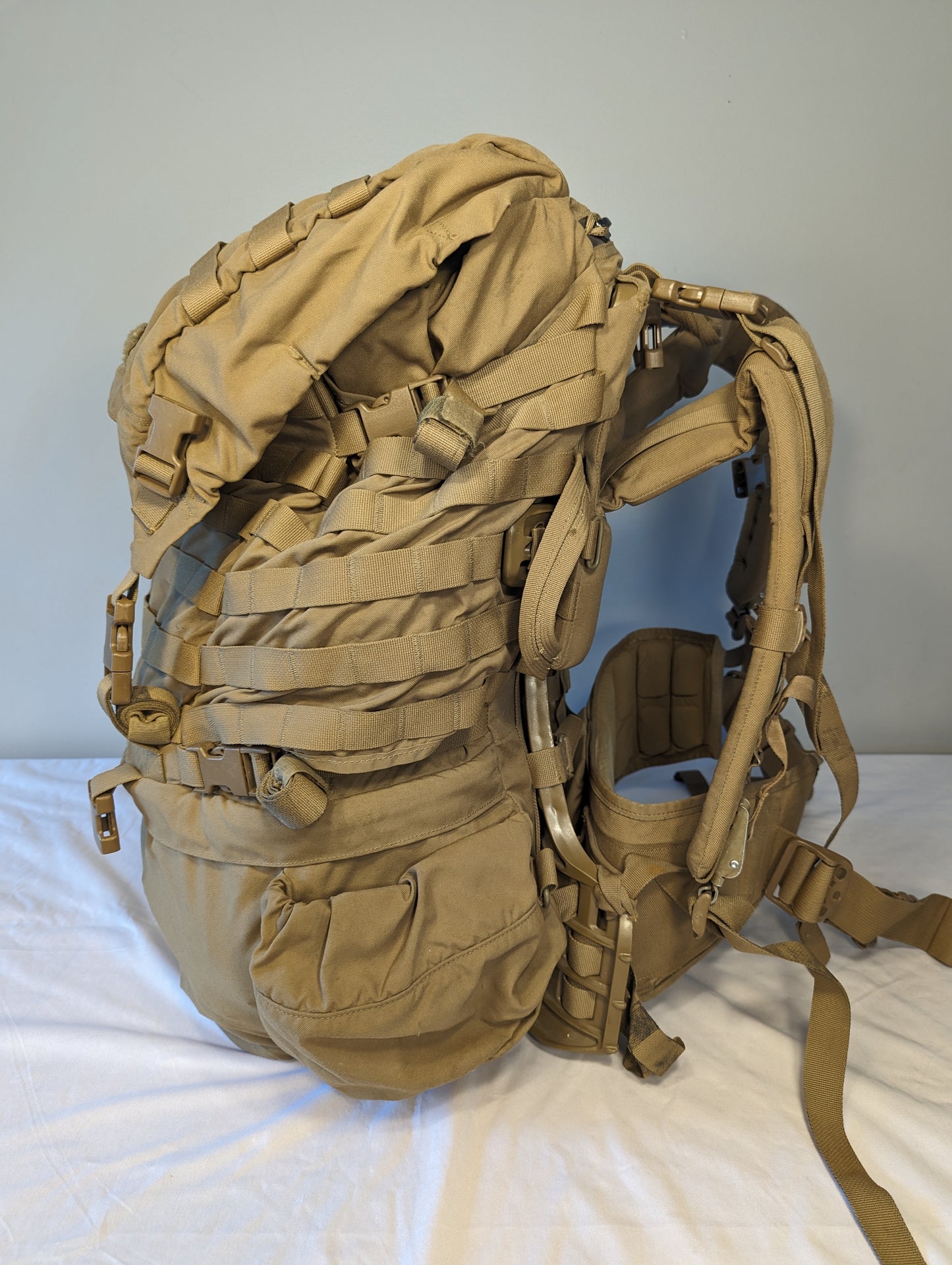 Tan military-style backpack on a white surface with a light gray background