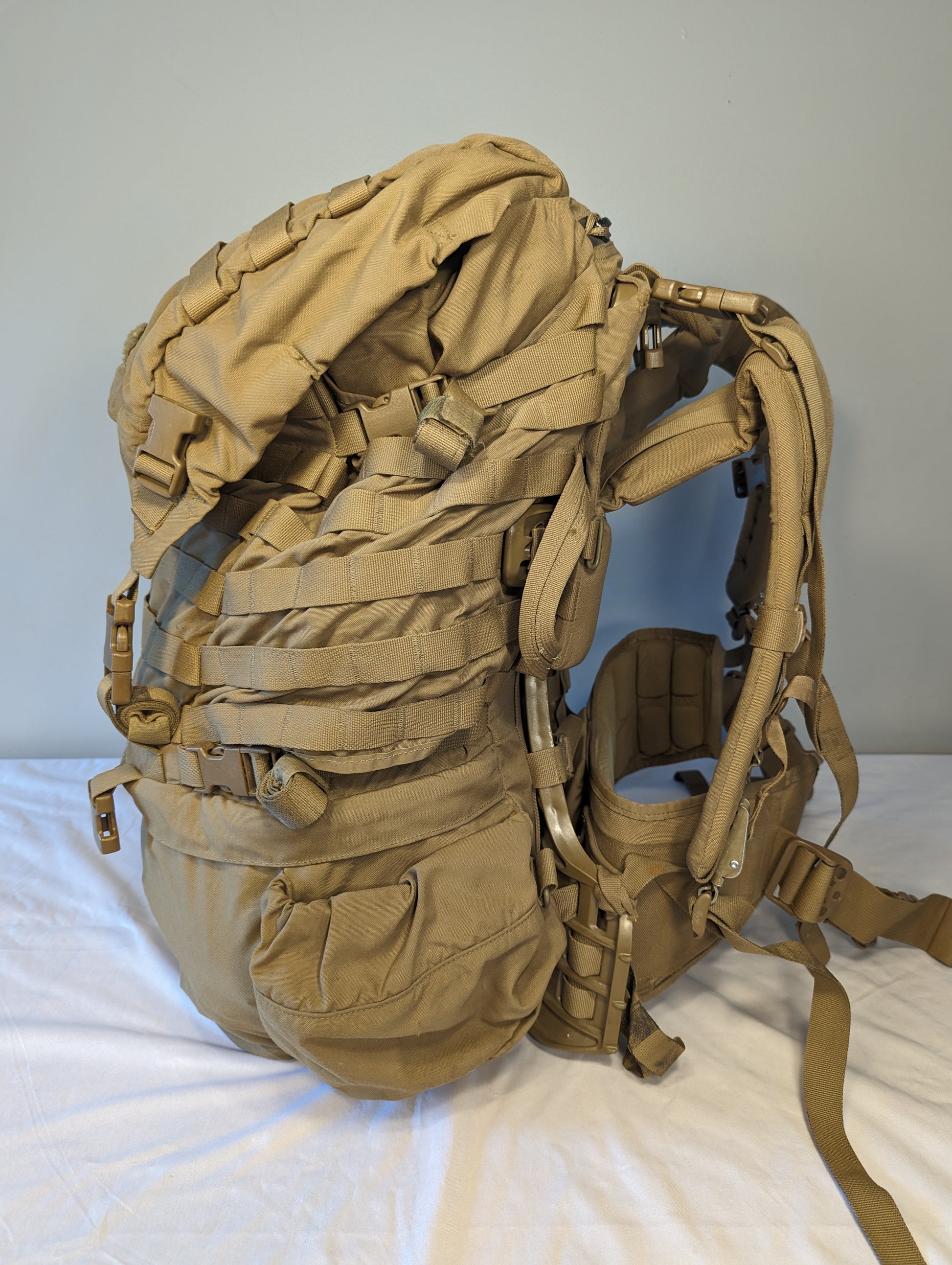 Tan military-style backpack on a white surface with a light gray background