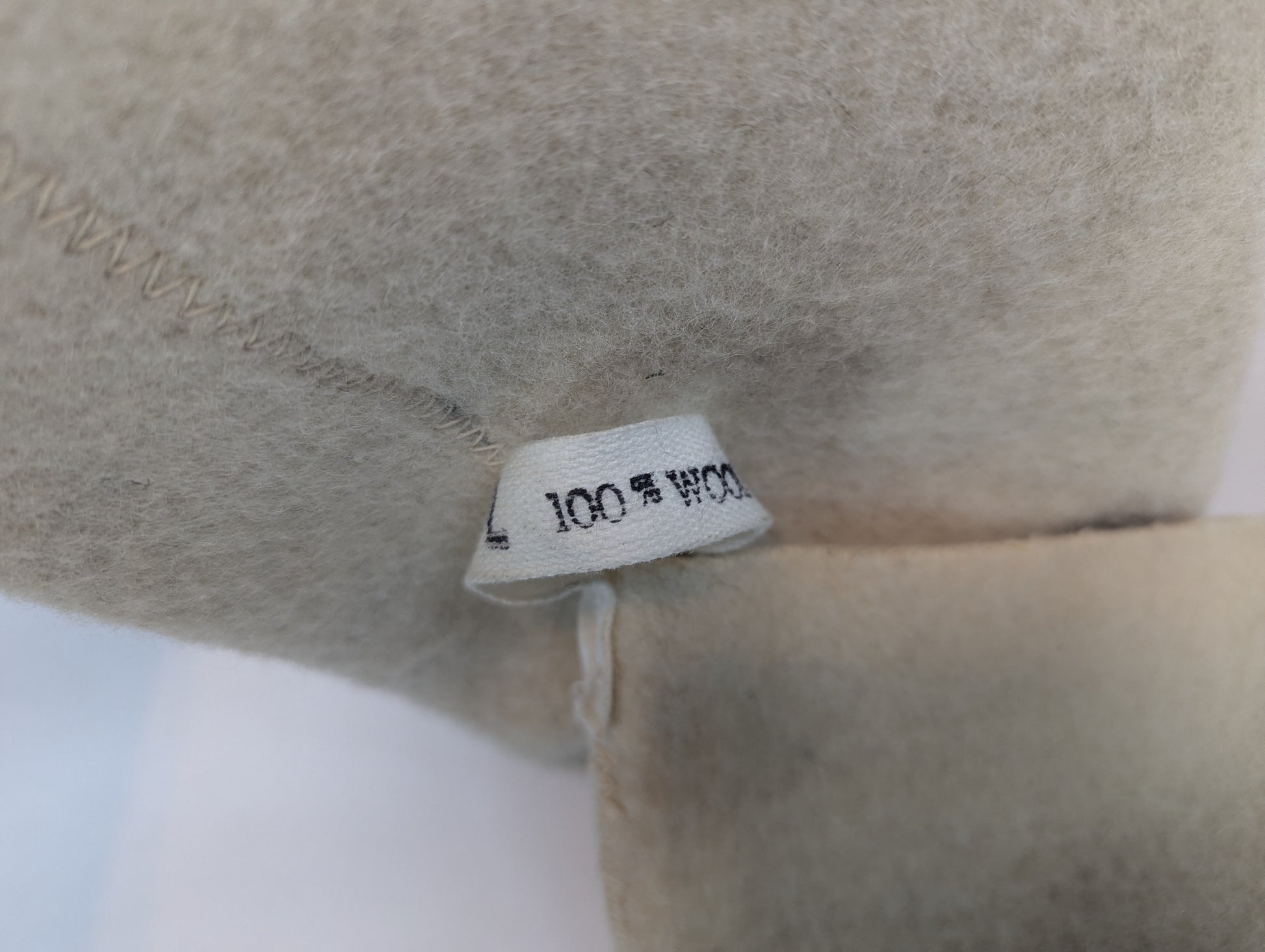 Close-up of a beige fabric with a label indicating '100% Wool'.