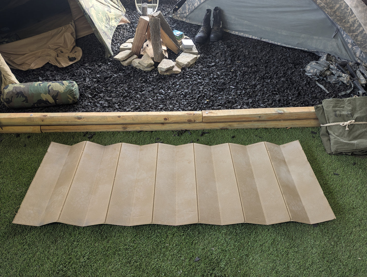 Beige sleeping pad on grass with camping setup in the background