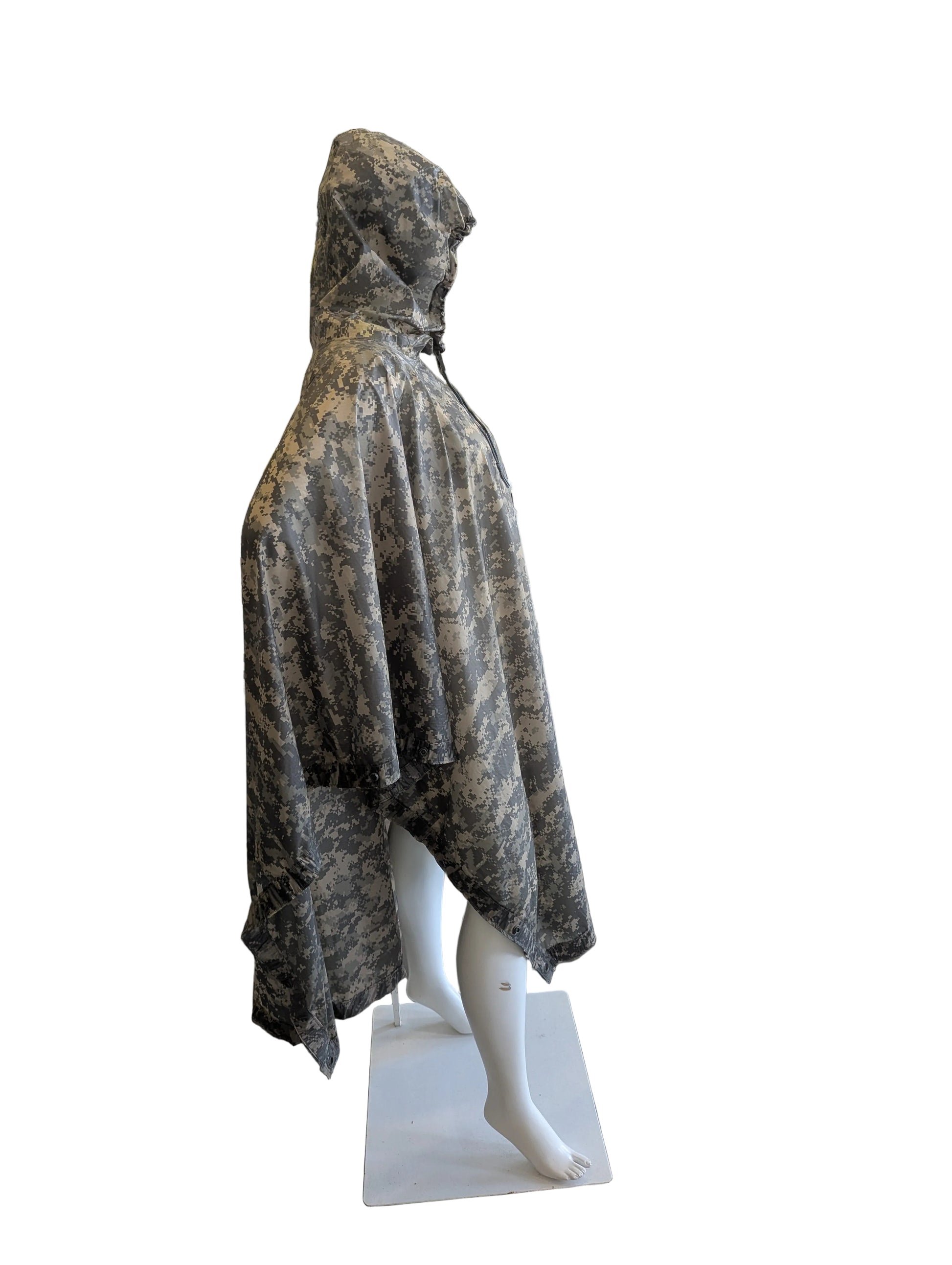Mannequin wearing a camouflage cape in front of a mural on a white brick wall.