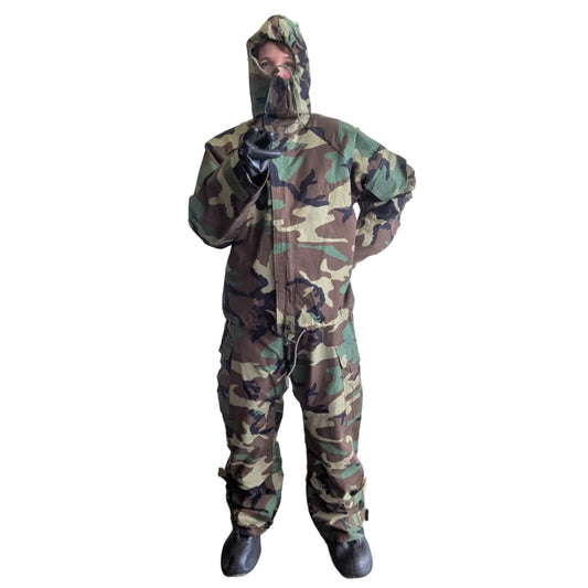 Person in camouflage snowsuit with gas mask in front of a mural with 'Fortitude' text.