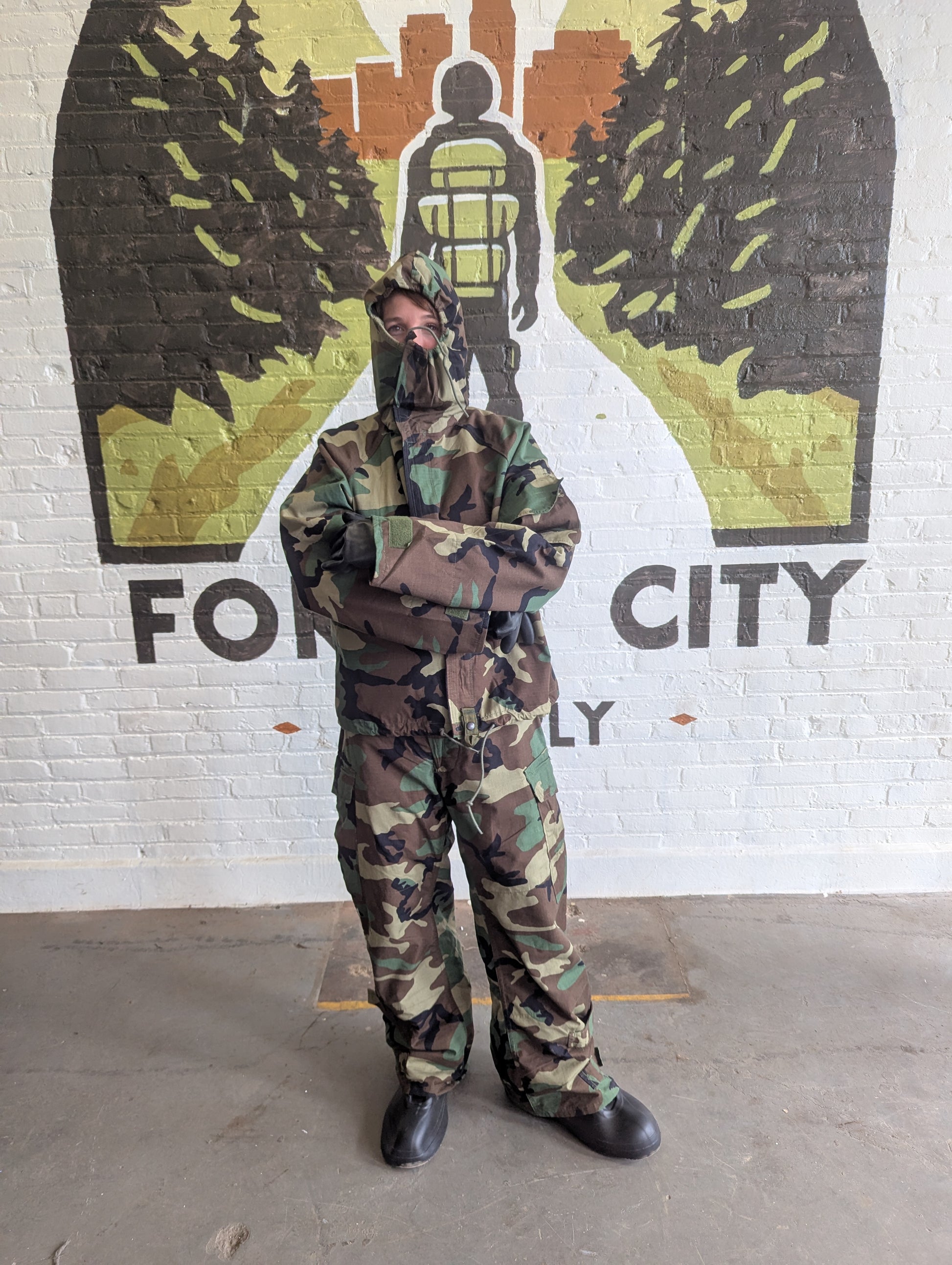 Person in camouflage outfit standing in front of a mural with 'For City' text.