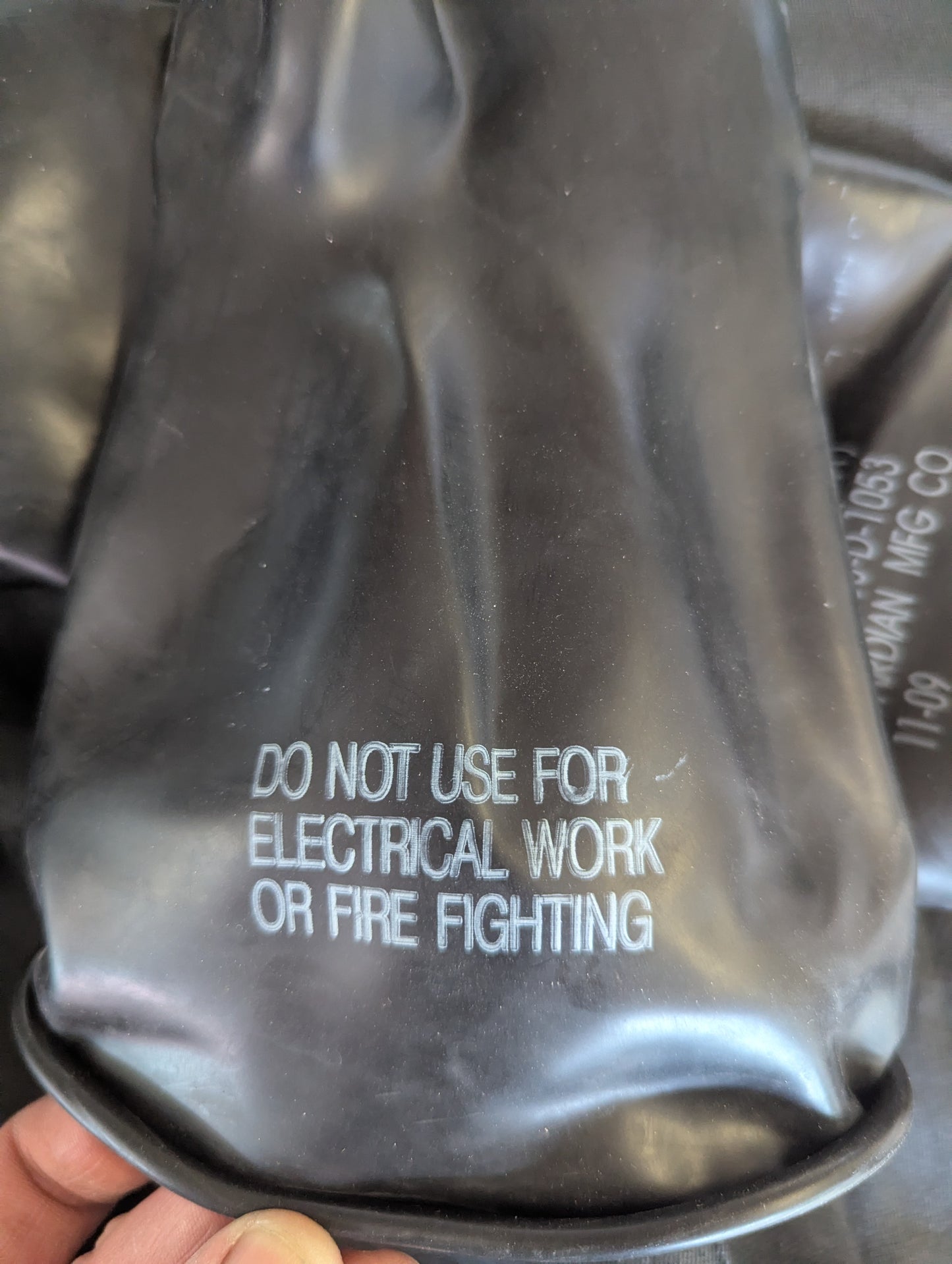Black rubber glove with warning text held by a hand