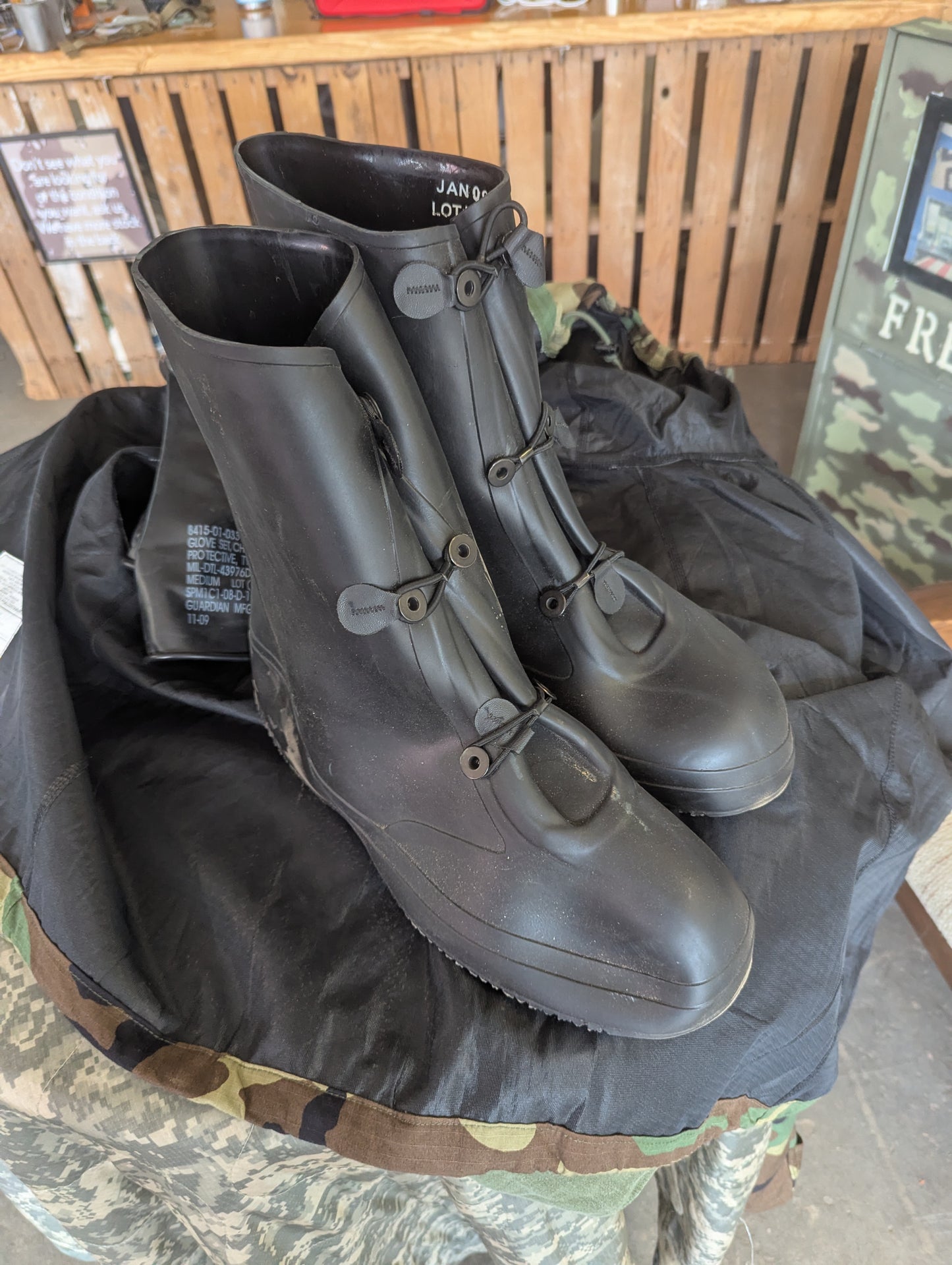 Pair of black rubber boots on a camouflage surface with a wooden background