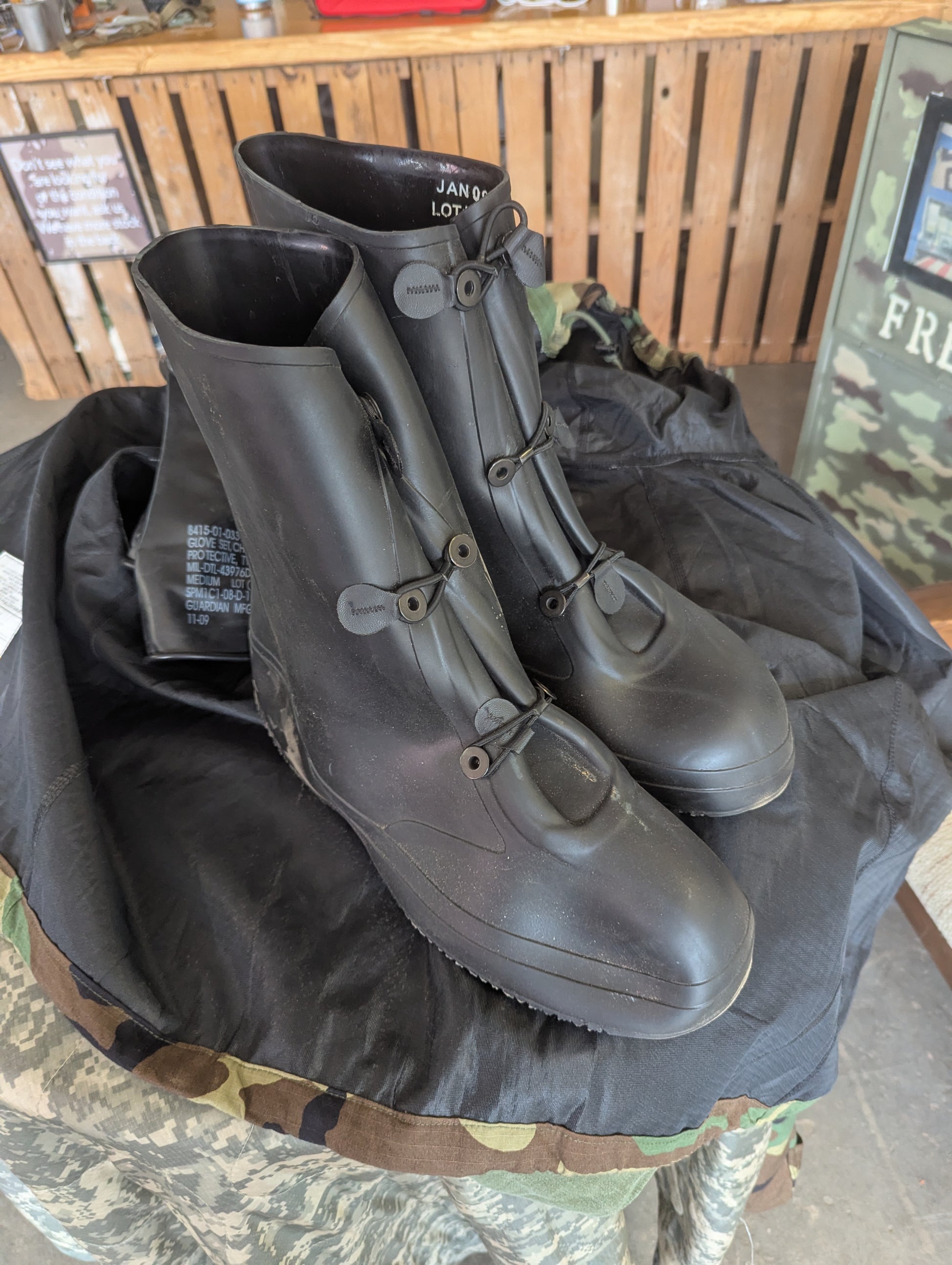 Pair of black rubber boots on a camouflage surface with a wooden background