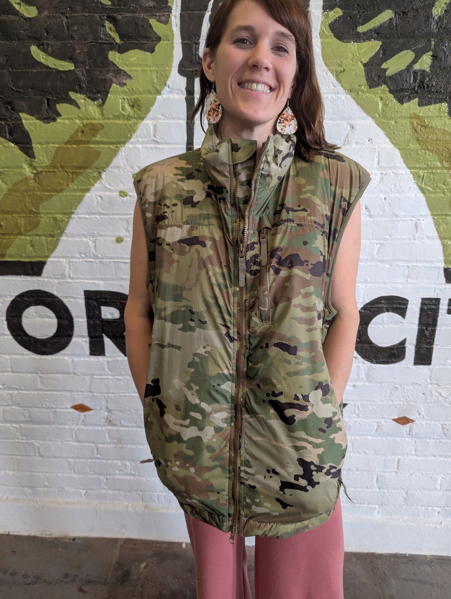 Woman wearing a camouflage vest in front of a mural.