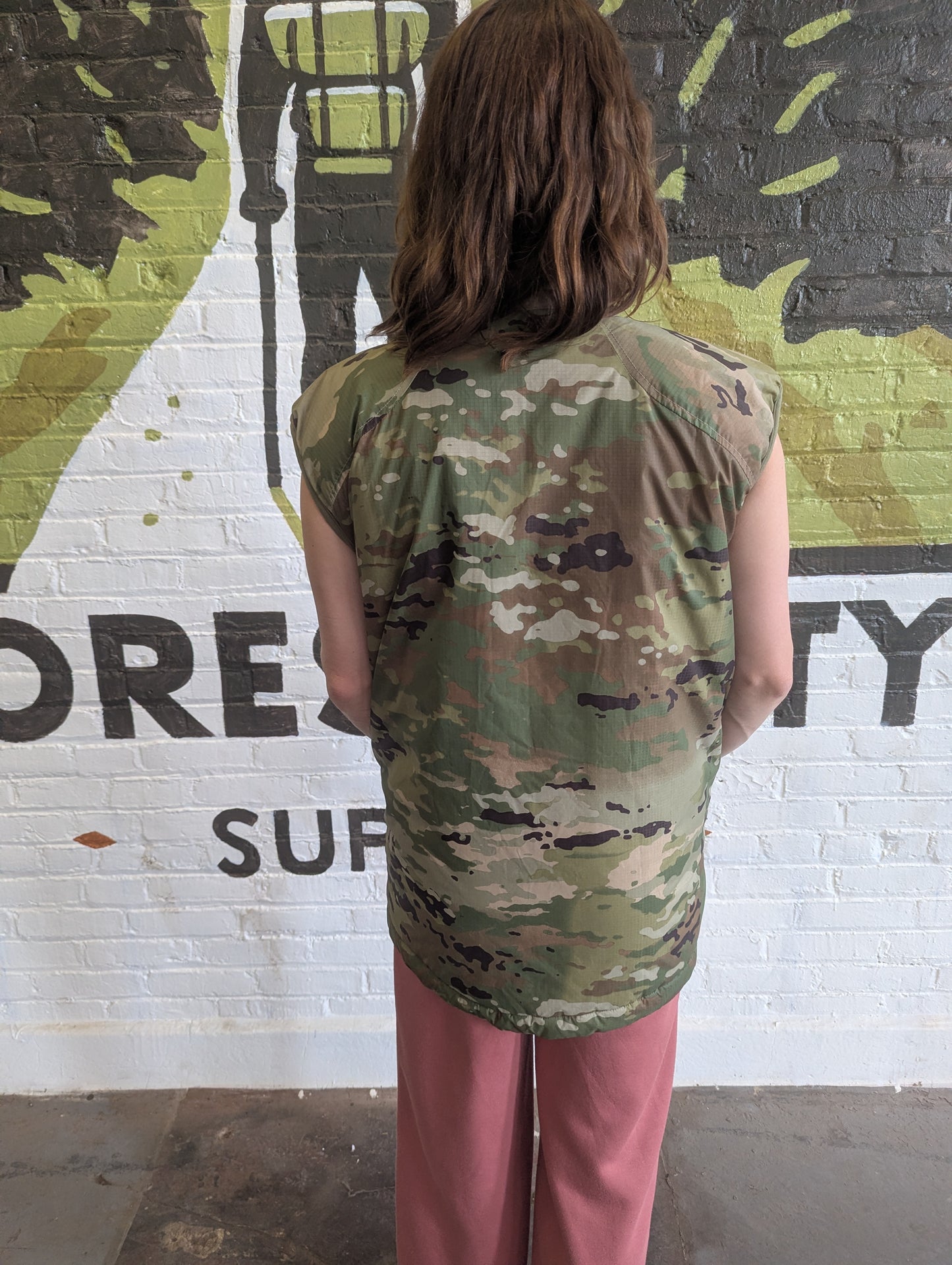 Person wearing a camouflage sleeveless top in front of a mural with text.