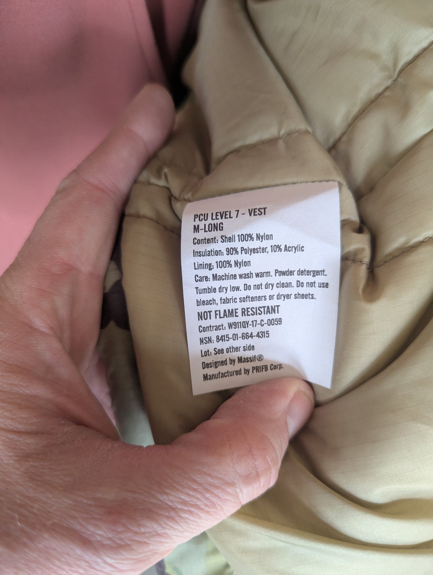 Hand holding a beige vest with a label on it