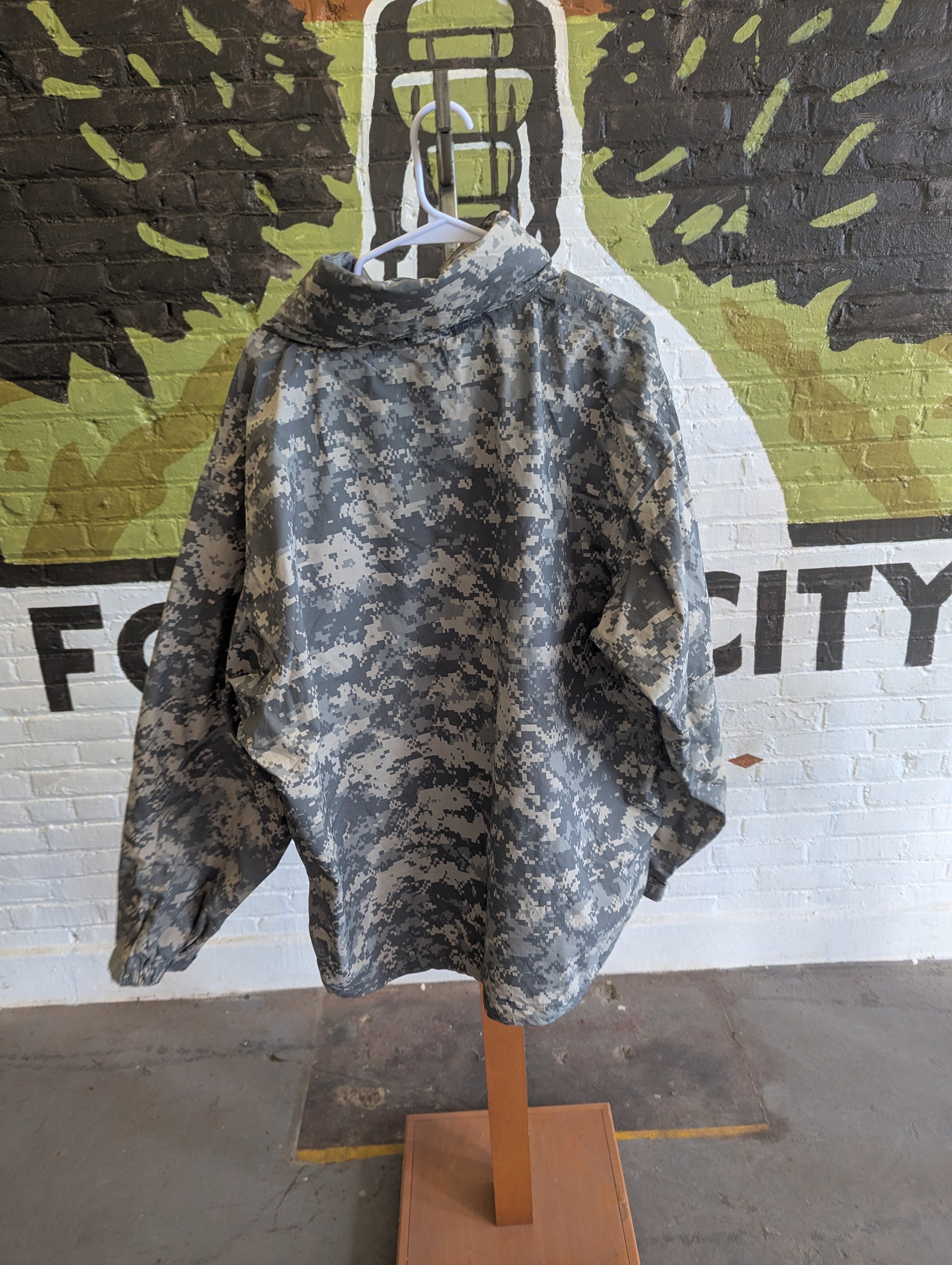 Camouflage-patterned jacket on a mannequin against a camouflage-patterned wall.