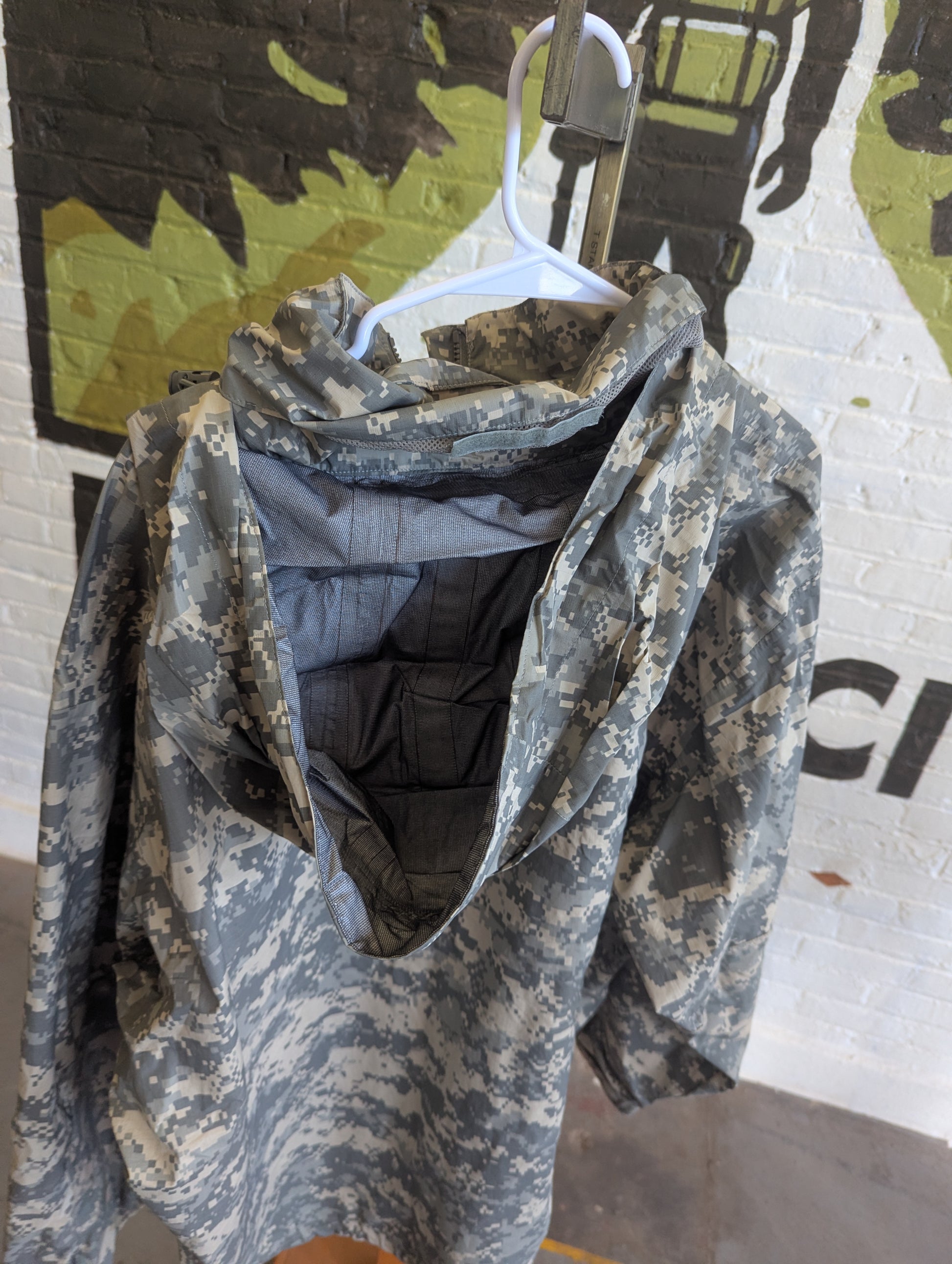 Camouflage-patterned jacket on a hanger against a camouflage wall.