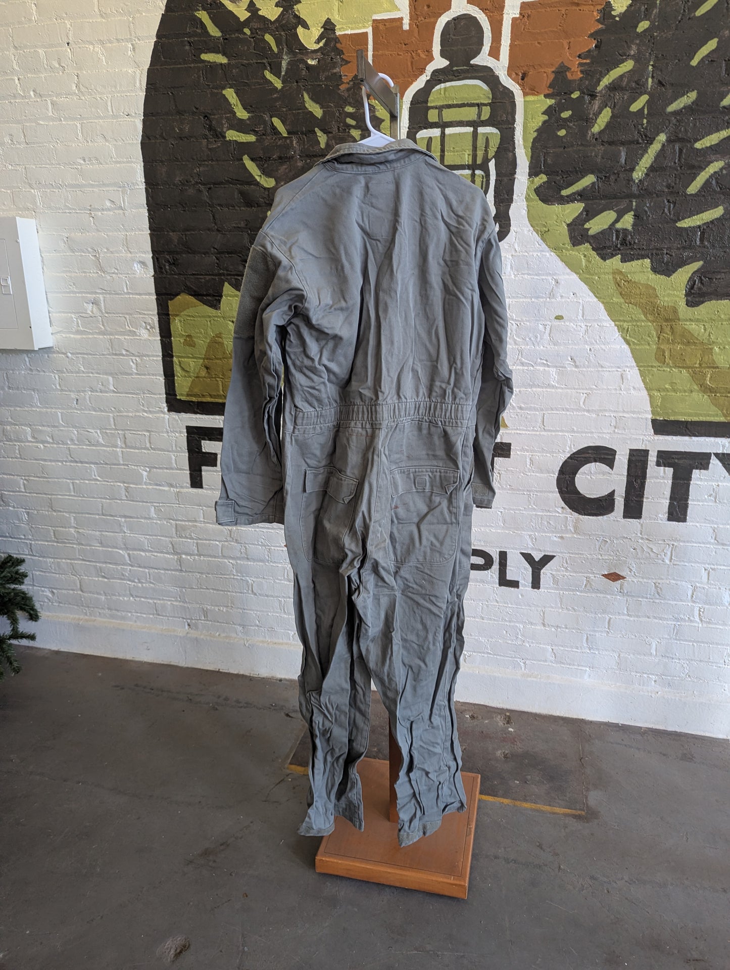 Gray jumpsuit on a mannequin in front of a mural with text and graphics.