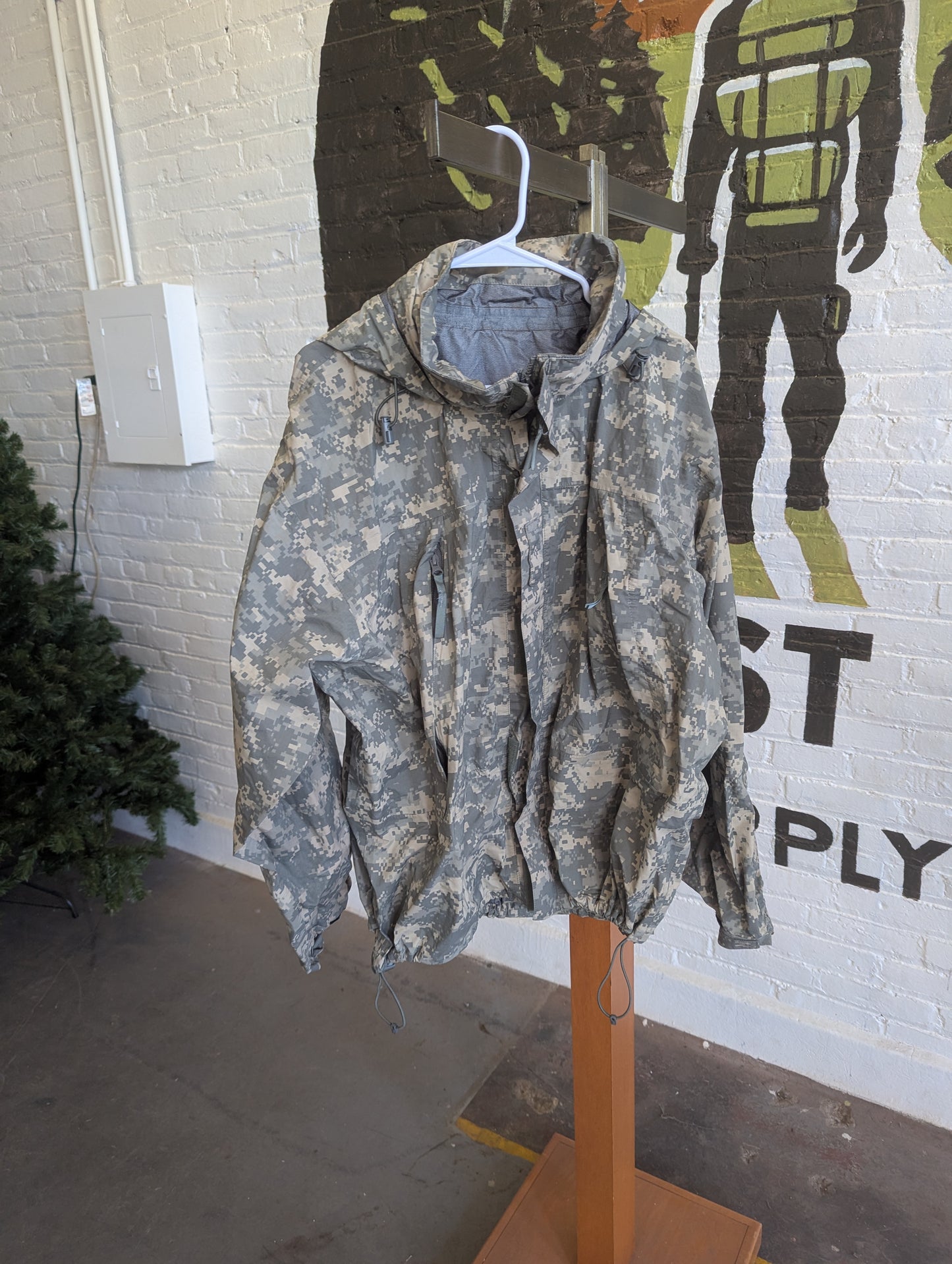 Camouflage jacket on a hanger against a wall with a graphic design.