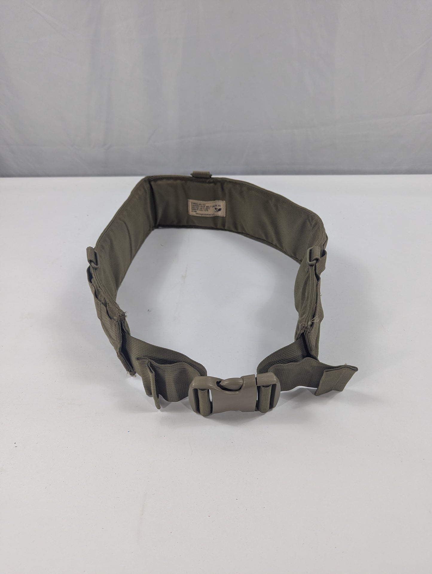An olive drab tactical belt with a quick-release plastic buckle, displayed on a white circular stand against a white fabric backdrop.