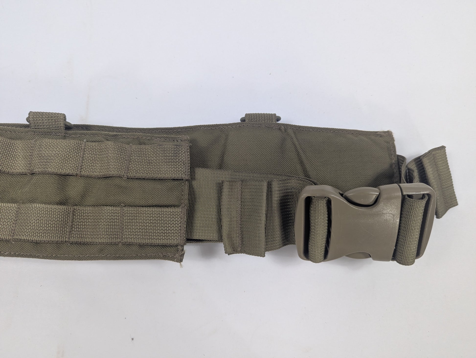 An olive drab tactical belt with a quick-release plastic buckle, displayed on a white circular stand against a white fabric backdrop.