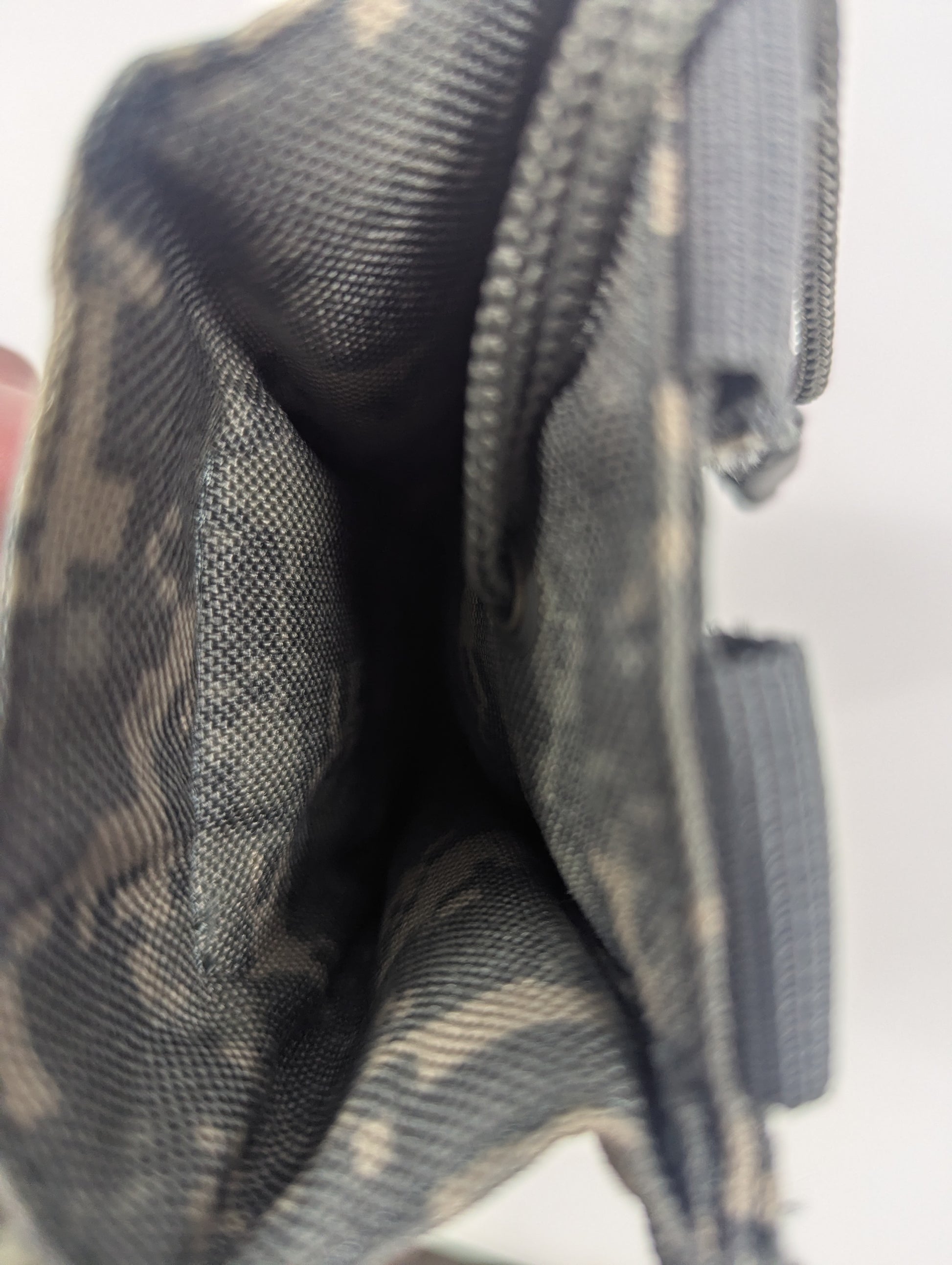 Close-up of a camouflage fabric zippered pouch or small bag, showing the interior lining and zipper detail against a light background.
