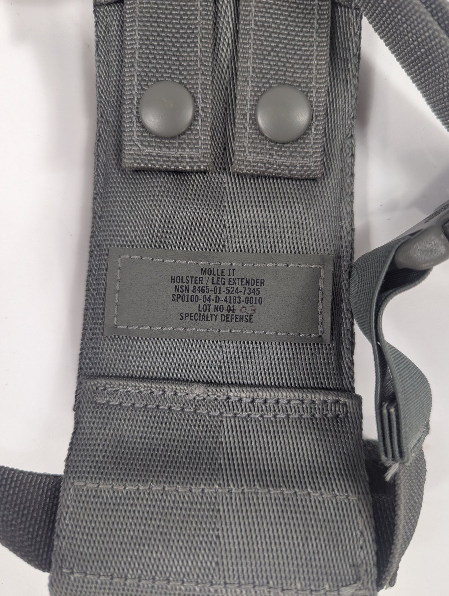 Close-up of a gray nylon MOLLE webbing harness or leg extender with two snap buttons and a central sewn label.