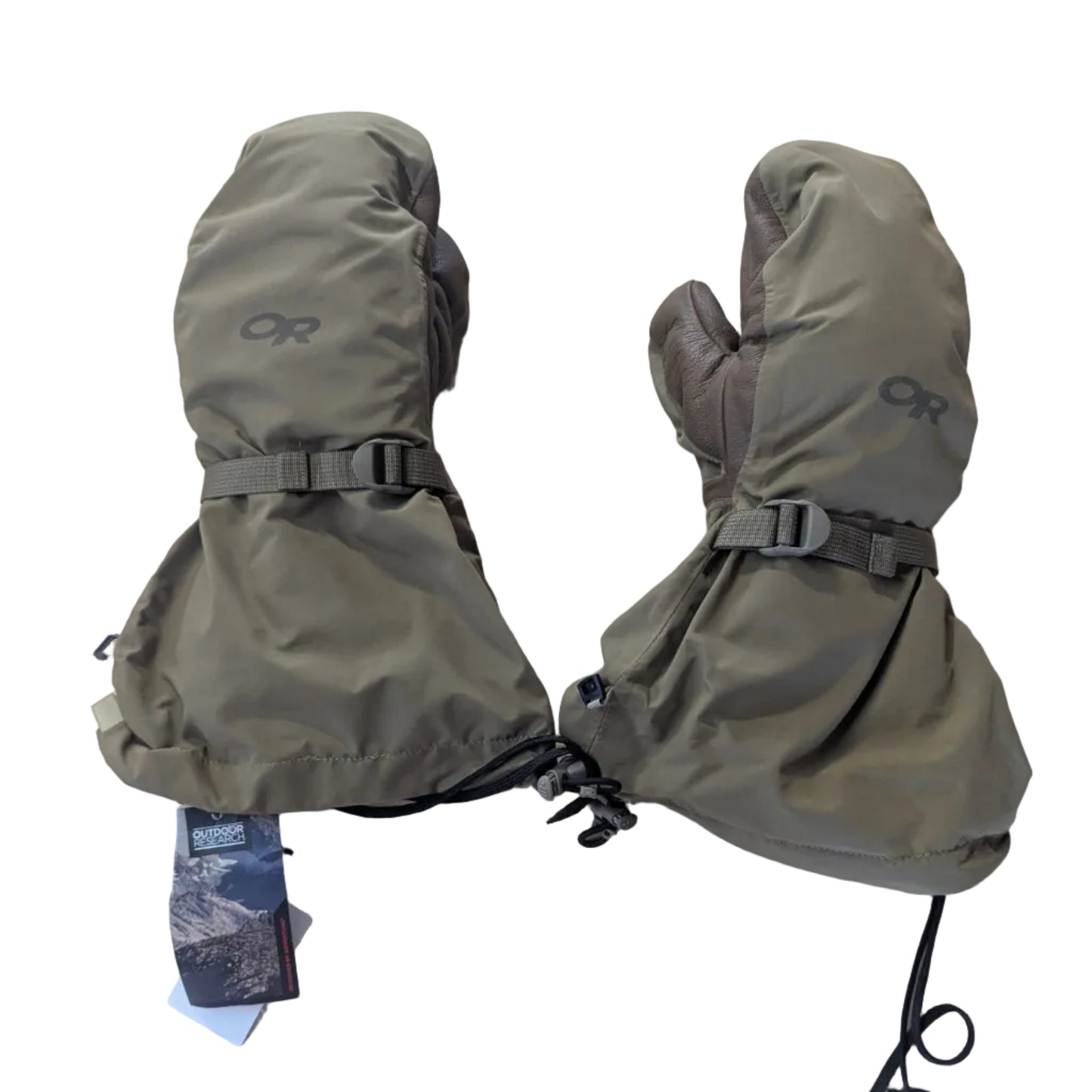 A pair of olive green outdoor mittens with drawstring cuffs and buckle straps, laid flat on a white surface. The brand logo 'OR' is visible on both mittens, and a product tag is attached to the left mitten.