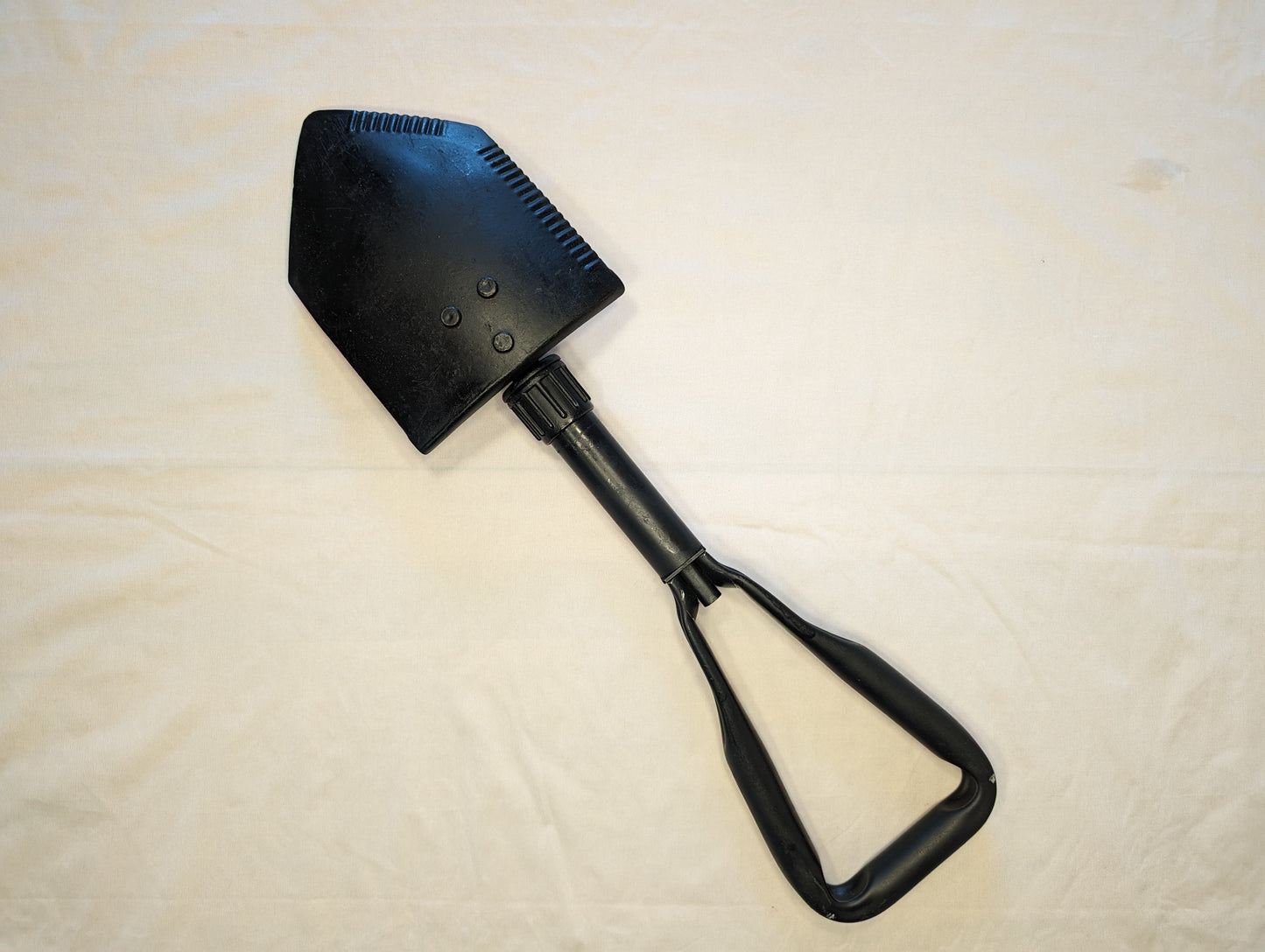 A used, black AMES Entrenching Tool (E-Tool) shown fully extended, displaying the long handle, the steel shovel blade with a serrated edge, and the black plastic D-handle.