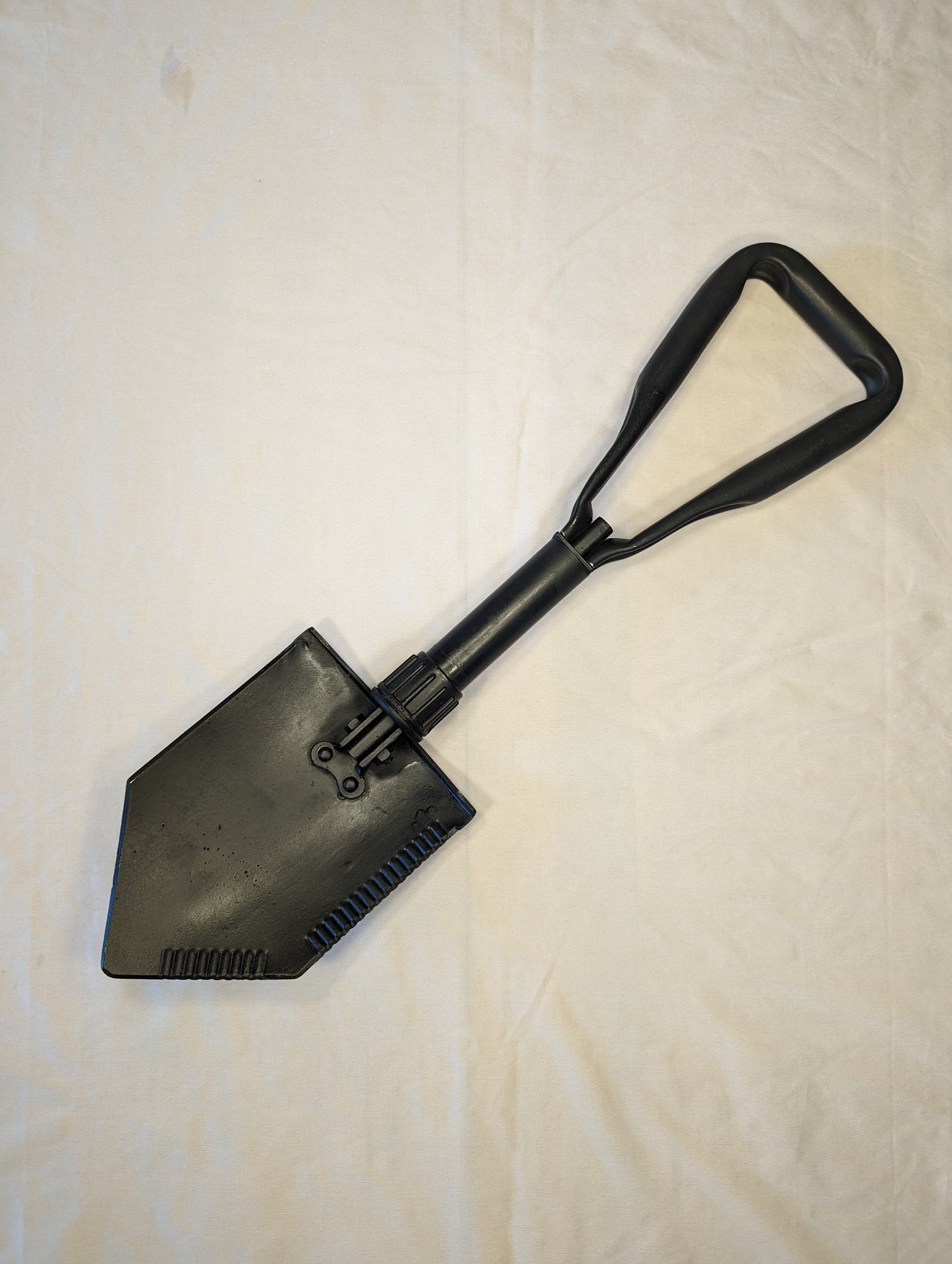 A used, black AMES Entrenching Tool (E-Tool) shown fully extended, displaying the long handle, the steel shovel blade with a serrated edge, and the black plastic D-handle.