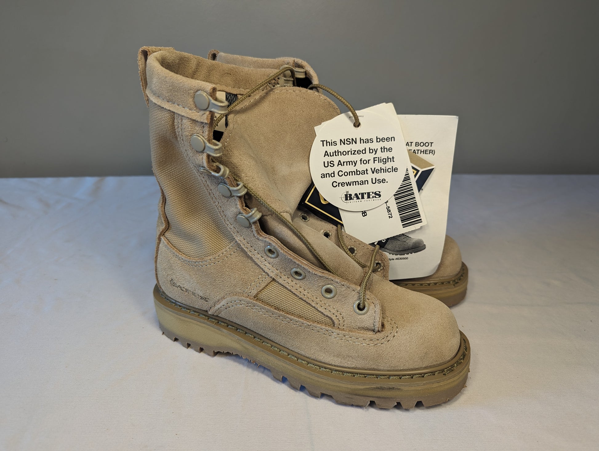 A single tan Bates Cold Weather Combat Boot, featuring a rough-out leather and nylon upper, speed lacing system, and a hang tag stating authorization for U.S. Army flight and combat vehicle crewman use.
