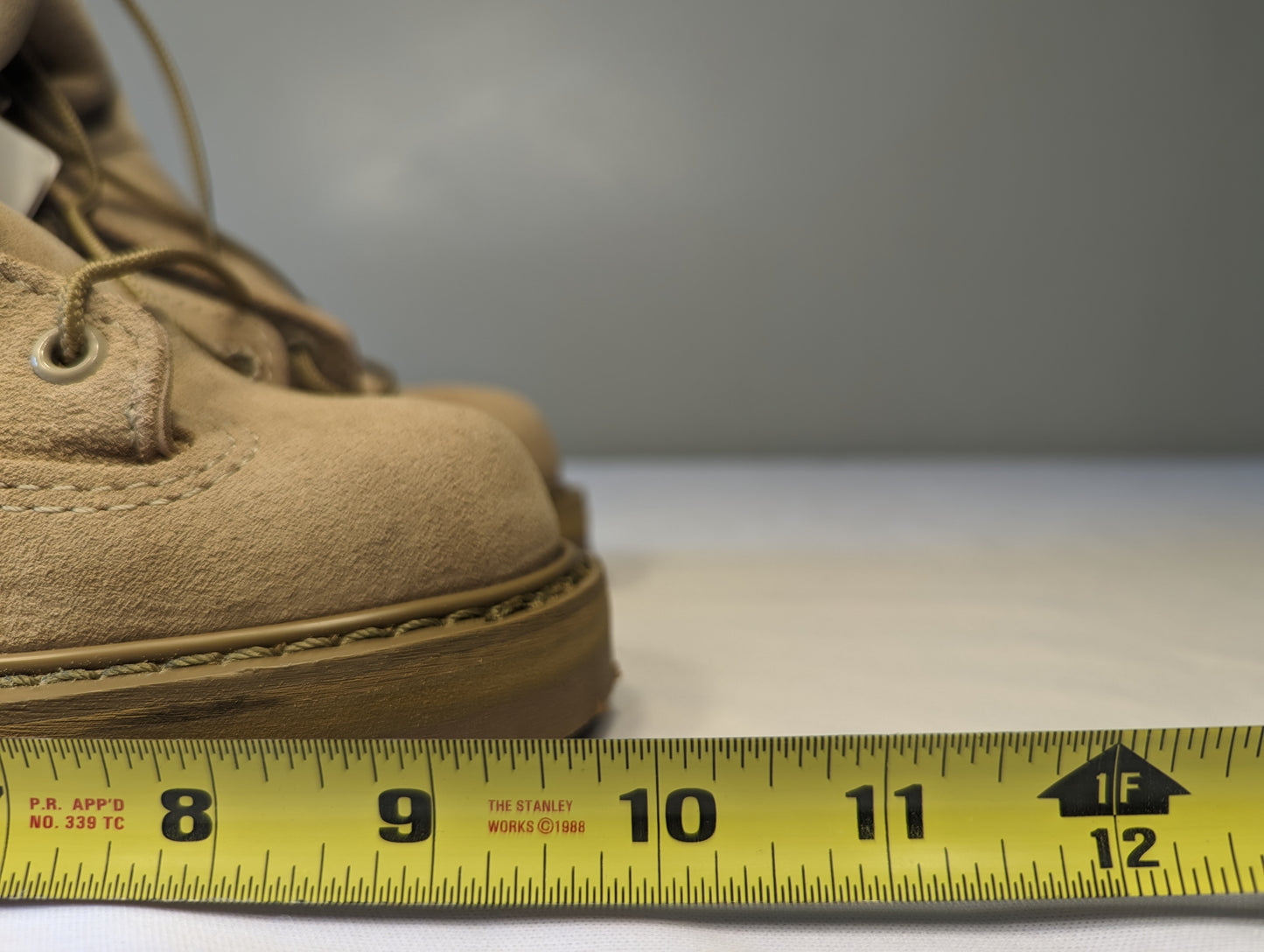 A close-up view of the tan suede toe box of a Bates Cold Weather Combat Boot, with a yellow Stanley tape measure placed across the sole to demonstrate the width measurement.