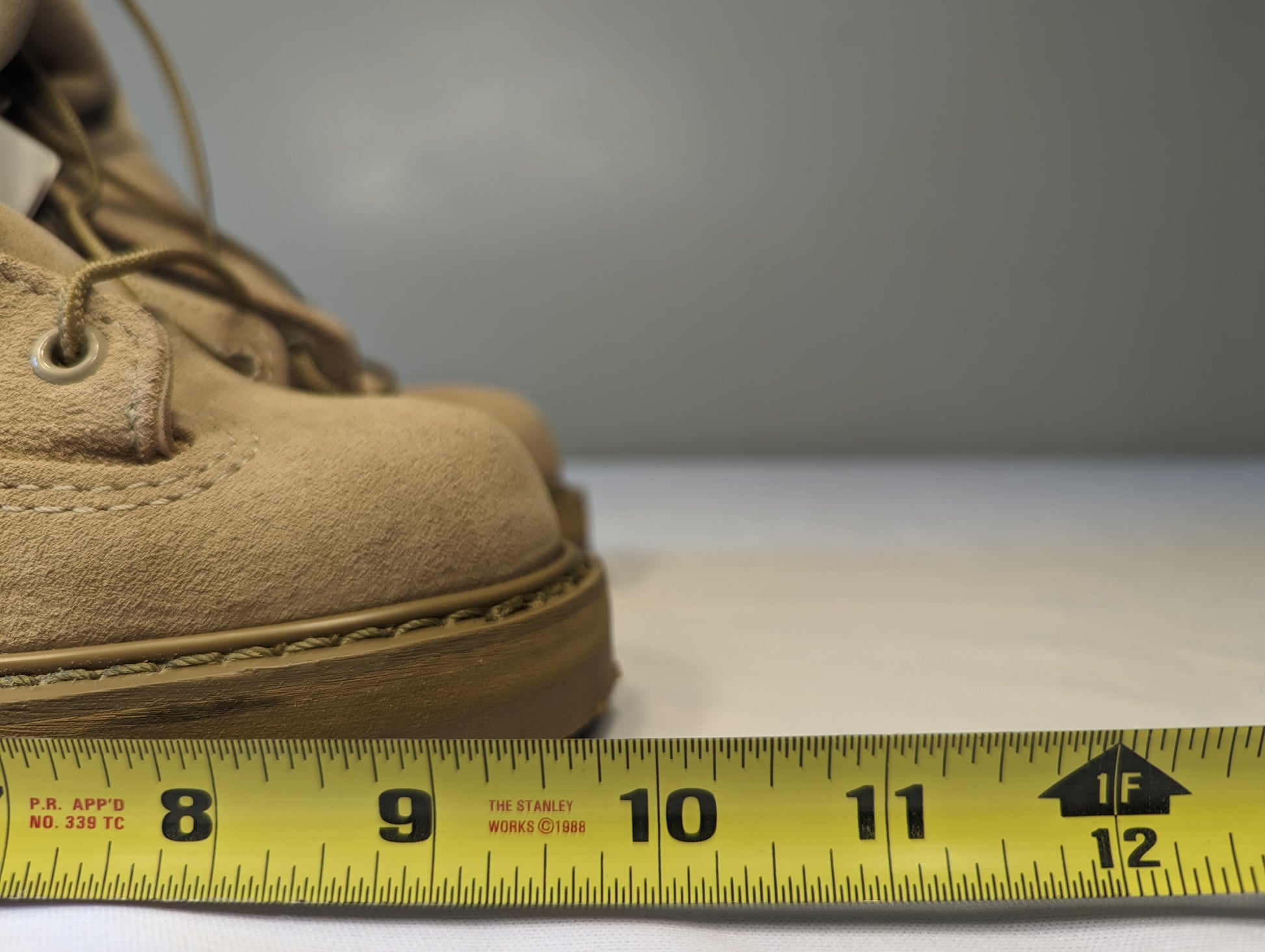 A close-up view of the tan suede toe box of a Bates Cold Weather Combat Boot, with a yellow Stanley tape measure placed across the sole to demonstrate the width measurement.