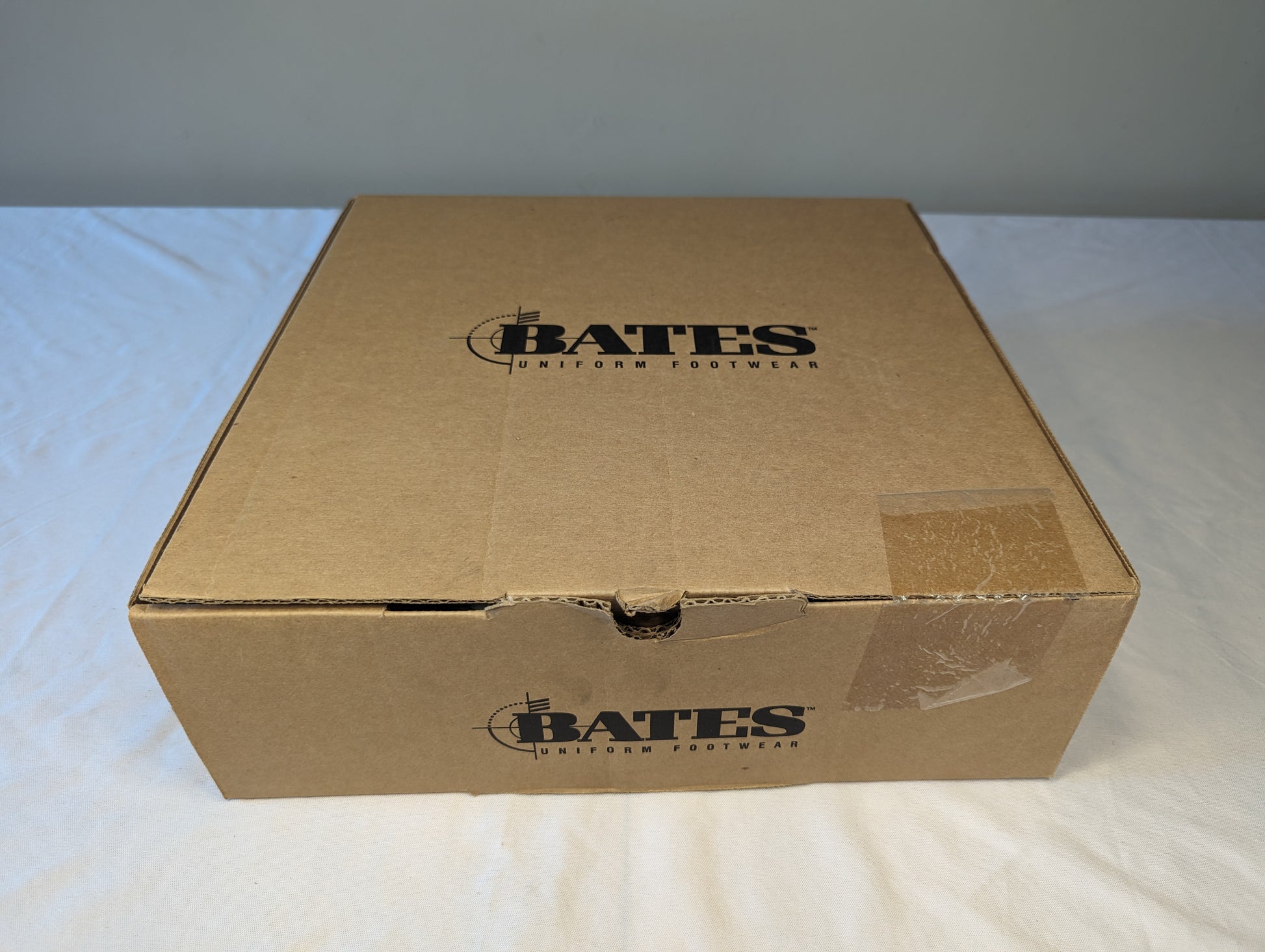 A closed brown cardboard Bates shoe box, sealed with clear packing tape and prominently displaying the 'BATES UNIFORM FOOTWEAR' logo on the top and front panel.