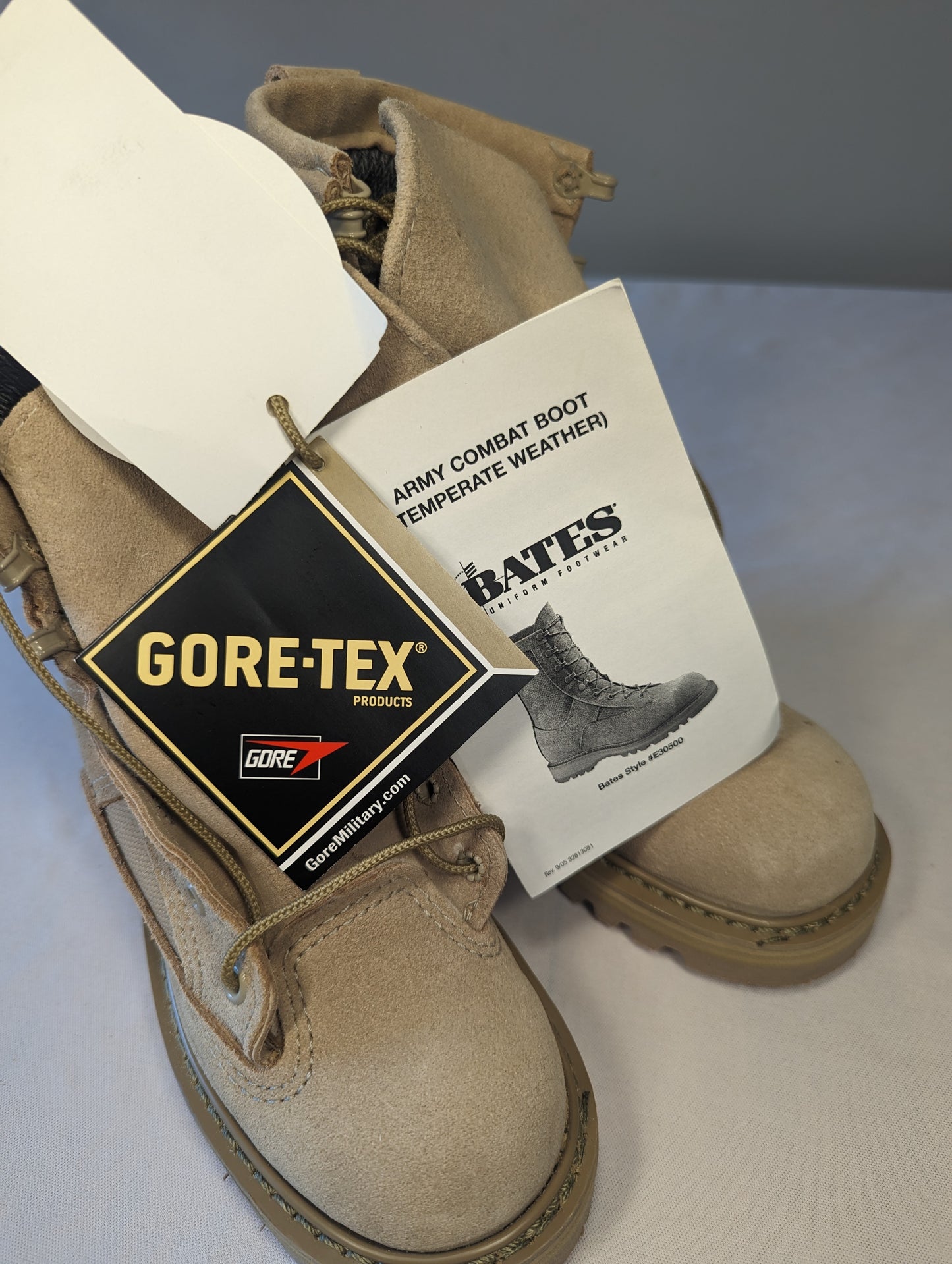 A pair of new tan Bates Cold Weather Combat Boots displayed on a white surface, featuring prominent Gore-Tex waterproof and military issue hang tags.
