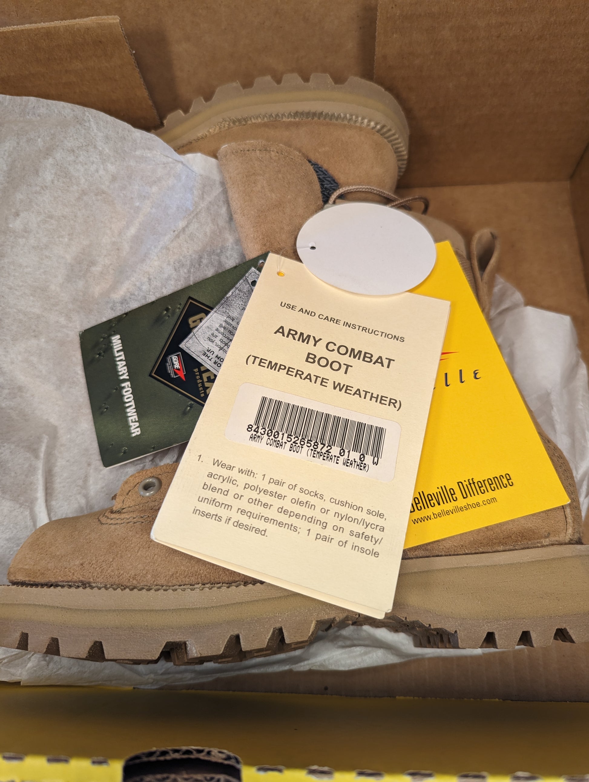 An overhead view inside an open cardboard box, showing a new tan Belleville Combat Boot, the yellow 'ARMY COMBAT BOOT (TEMPERATE WEATHER)' instruction card, and original tags.