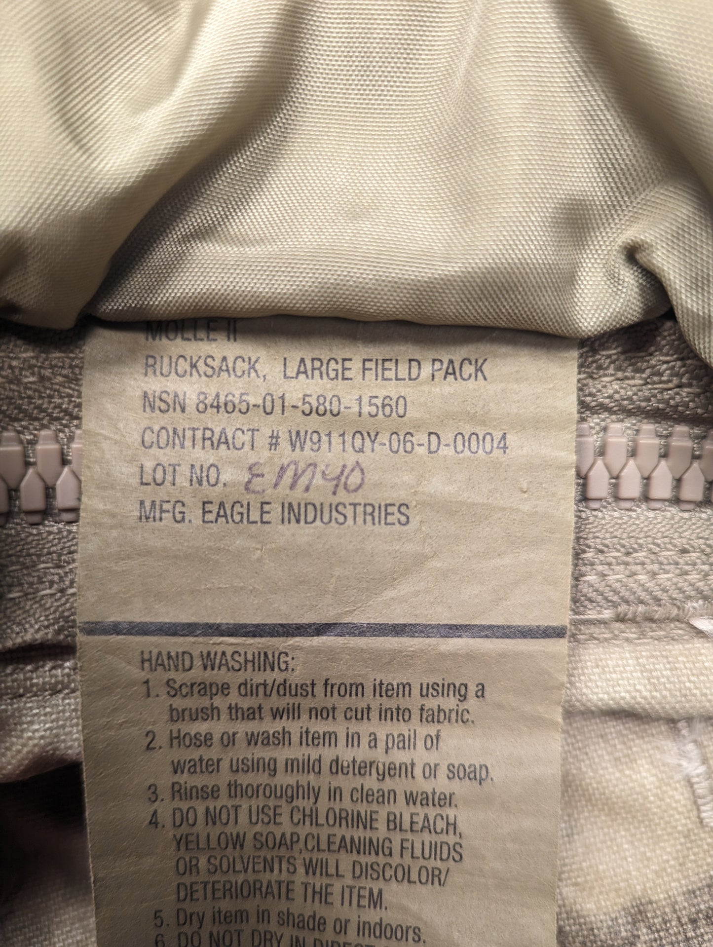 A close-up photograph of the official U.S. Military issue tag sewn into the Large Field Pack, clearly displaying the product name, NSN 8465-01-580-1560, manufacturer 'EAGLE INDUSTRIES', and detailed hand washing instructions.
