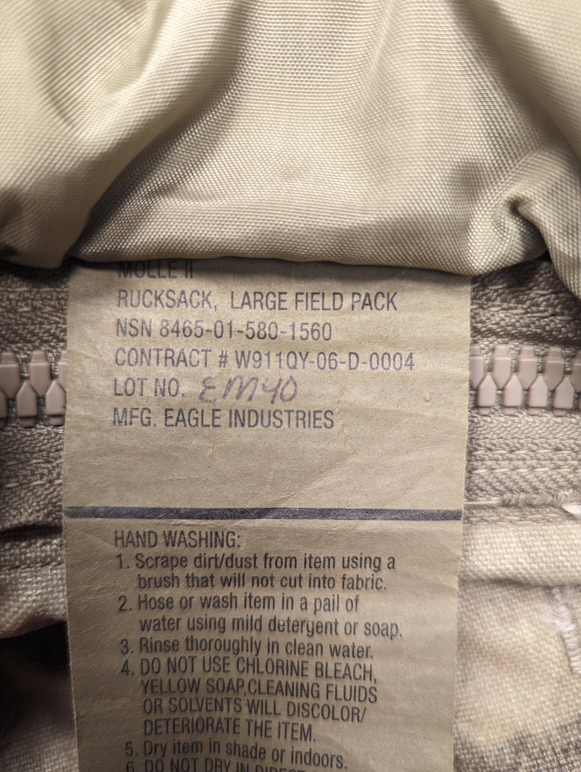 A close-up photograph of the official U.S. Military issue tag sewn into the Large Field Pack, clearly displaying the product name, NSN 8465-01-580-1560, manufacturer 'EAGLE INDUSTRIES', and detailed hand washing instructions.