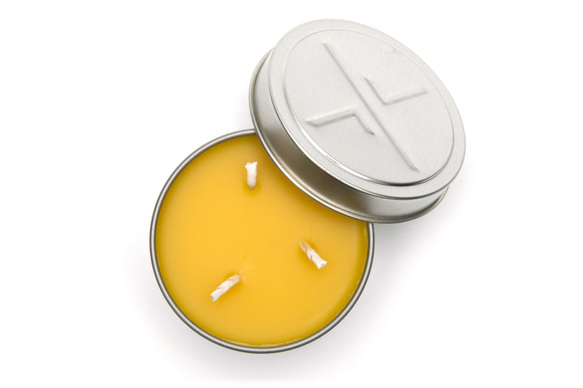 An overhead studio shot of a large, open candleTIN revealing the smooth yellow beeswax and three short wicks, with the embossed lid resting next to the tin on a white background.