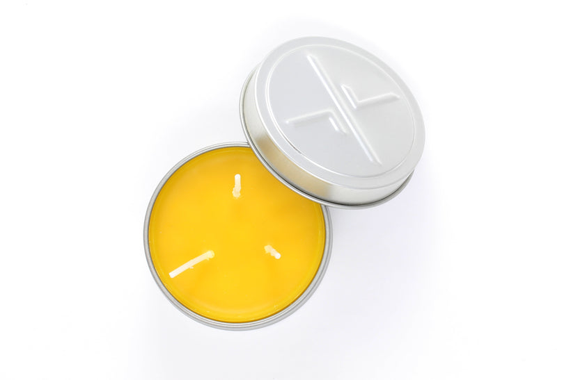 An overhead studio shot of a large, open candleTIN, showing the smooth yellow beeswax and three wicks, with the embossed lid resting next to the tin on a white background.