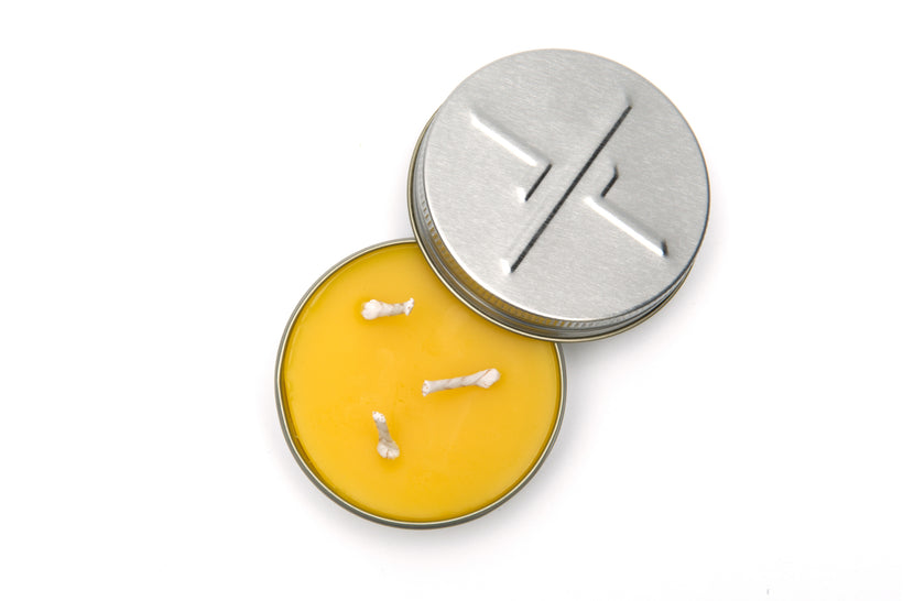 An overhead studio shot of a small, open candleTIN revealing the smooth yellow beeswax and three short wicks, with the embossed lid resting next to the tin on a white background.