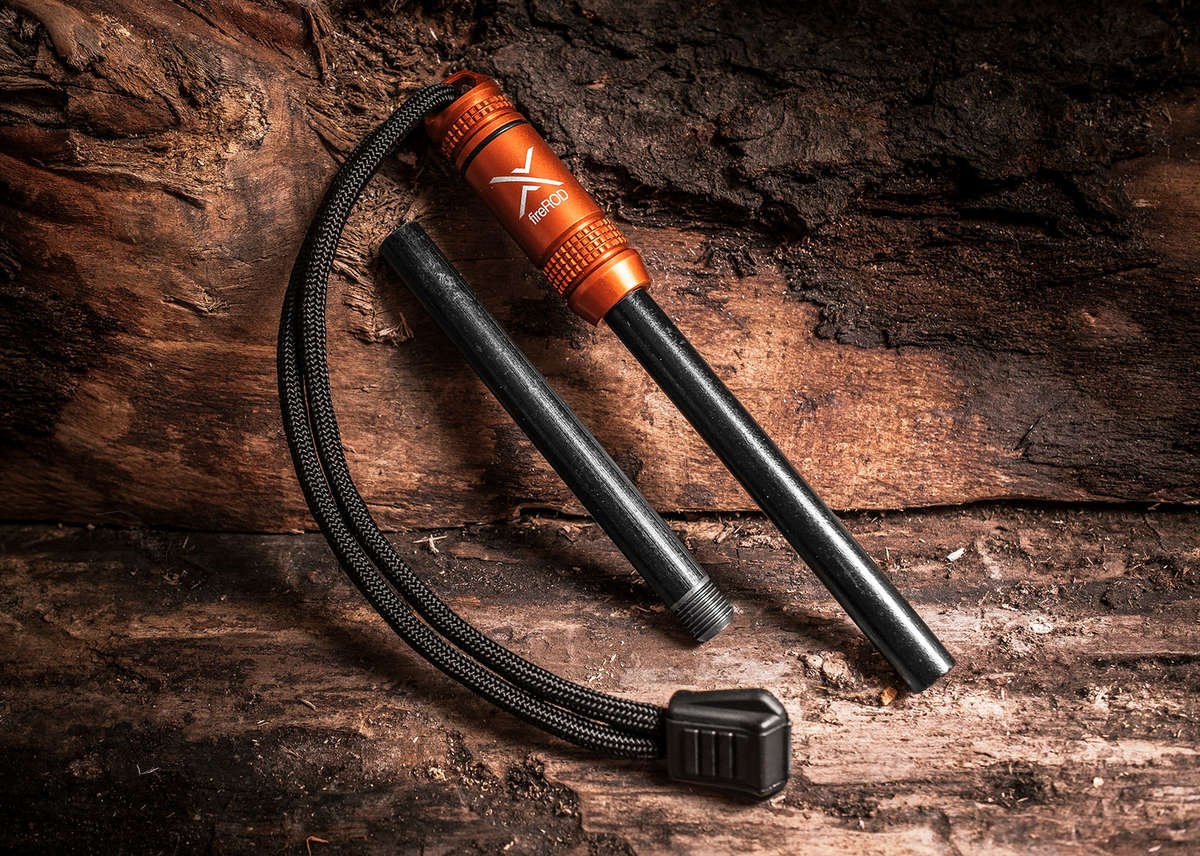A close-up of the orange fireROD fire starter disassembled, showing the anodized aluminum handle and the black ferrocerium rod, resting on a dark, heavily textured wooden surface.