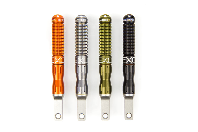 A studio shot showing four nanoSTRIKER XL fire starters standing upright in a row on a white background, demonstrating the available colors: orange, silver/gunmetal, olive green, and black.