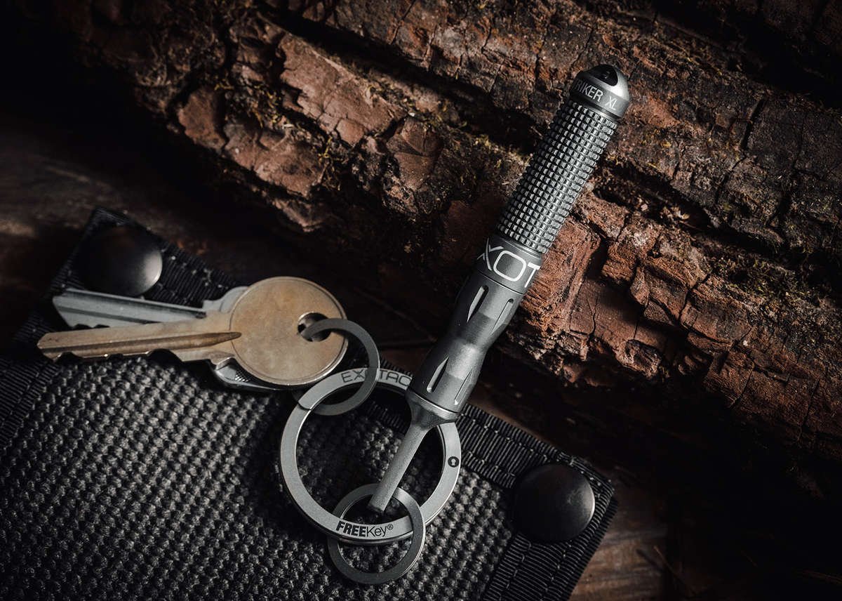 A black nanoSTRIKER XL fire starter resting on a dark, textured surface, attached to a metal keyring with a house key and a second metal tag, emphasizing its use as an an everyday carry item.