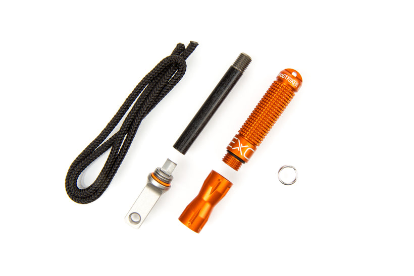 An exploded view of the orange nanoSTRIKER XL fire starter, showing all components: the anodized aluminum handle, the ferrocerium rod, the black striker, and the paracord lanyard, all displayed on a white background.
